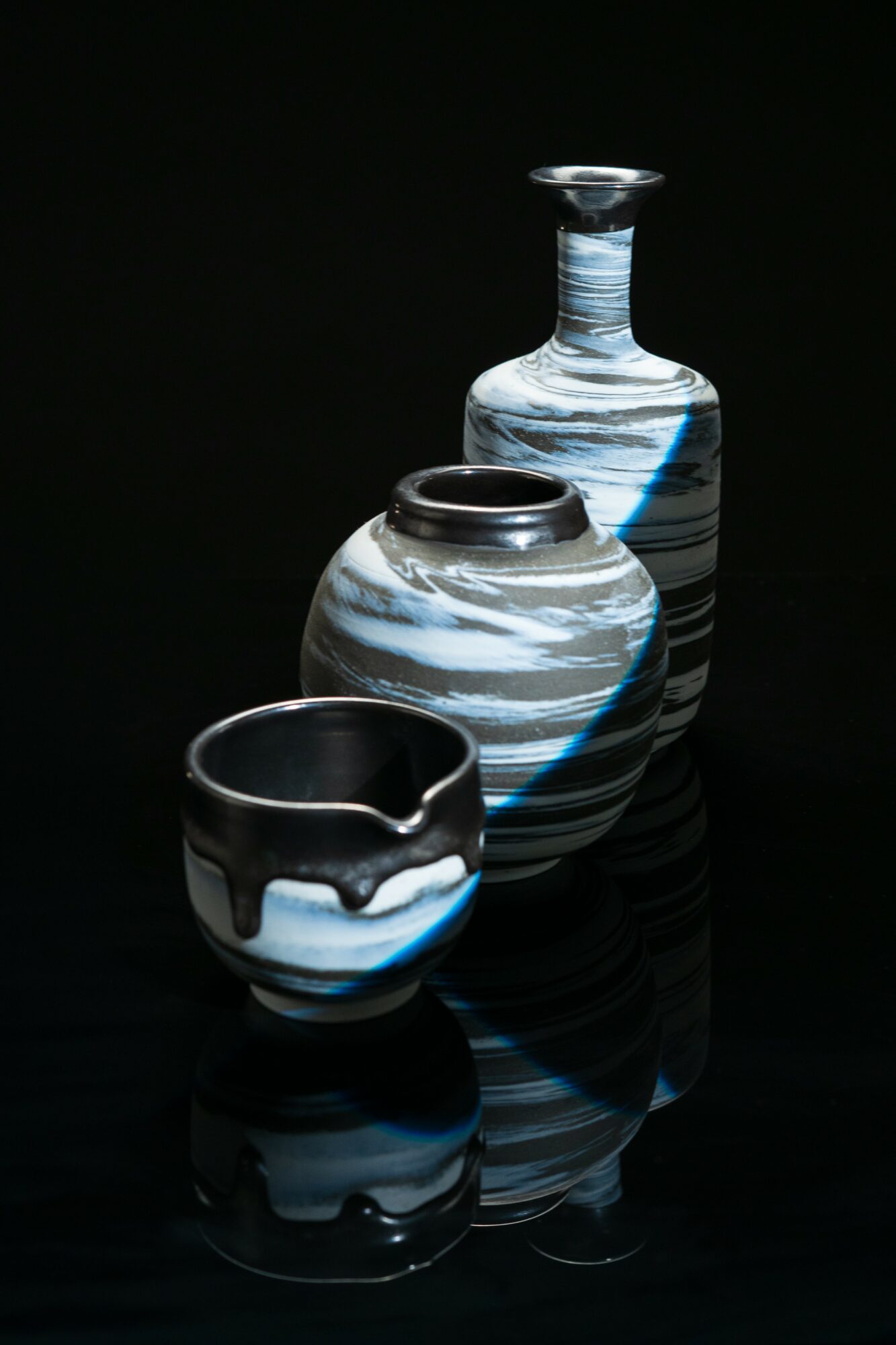 Three glass vases with blue, white, and black swirled patterns on a reflective black surface.