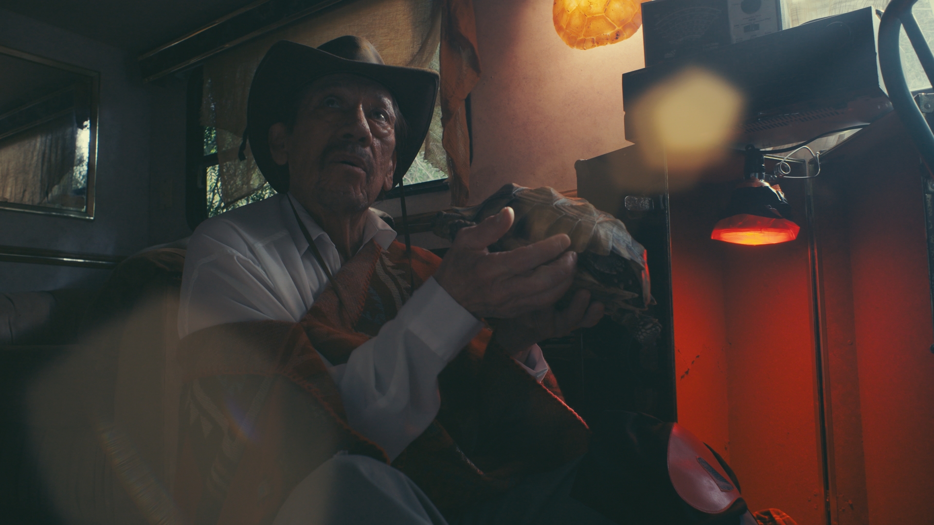 Person wearing a hat sitting inside a dimly lit space, holding an object with a blurred background.