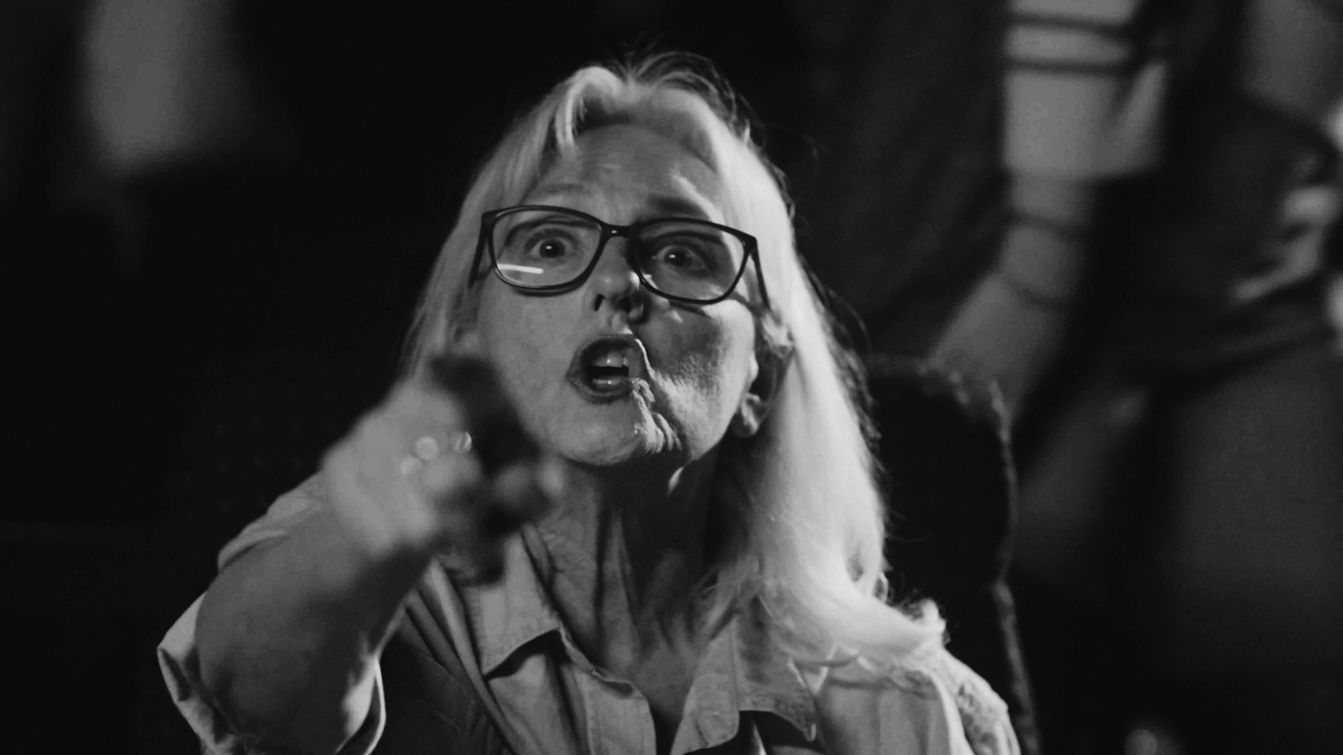 Woman with glasses and long hair pointing forward, appearing angry or upset, in black and white.