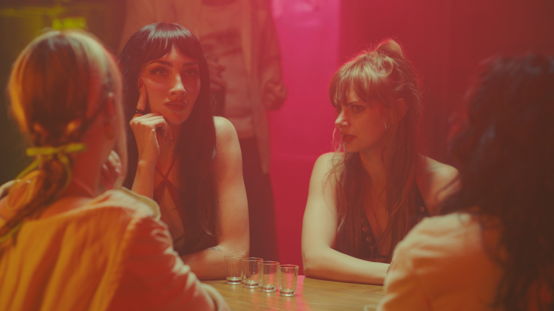 Four women sitting at a table in a dimly lit setting, engaging in conversation.