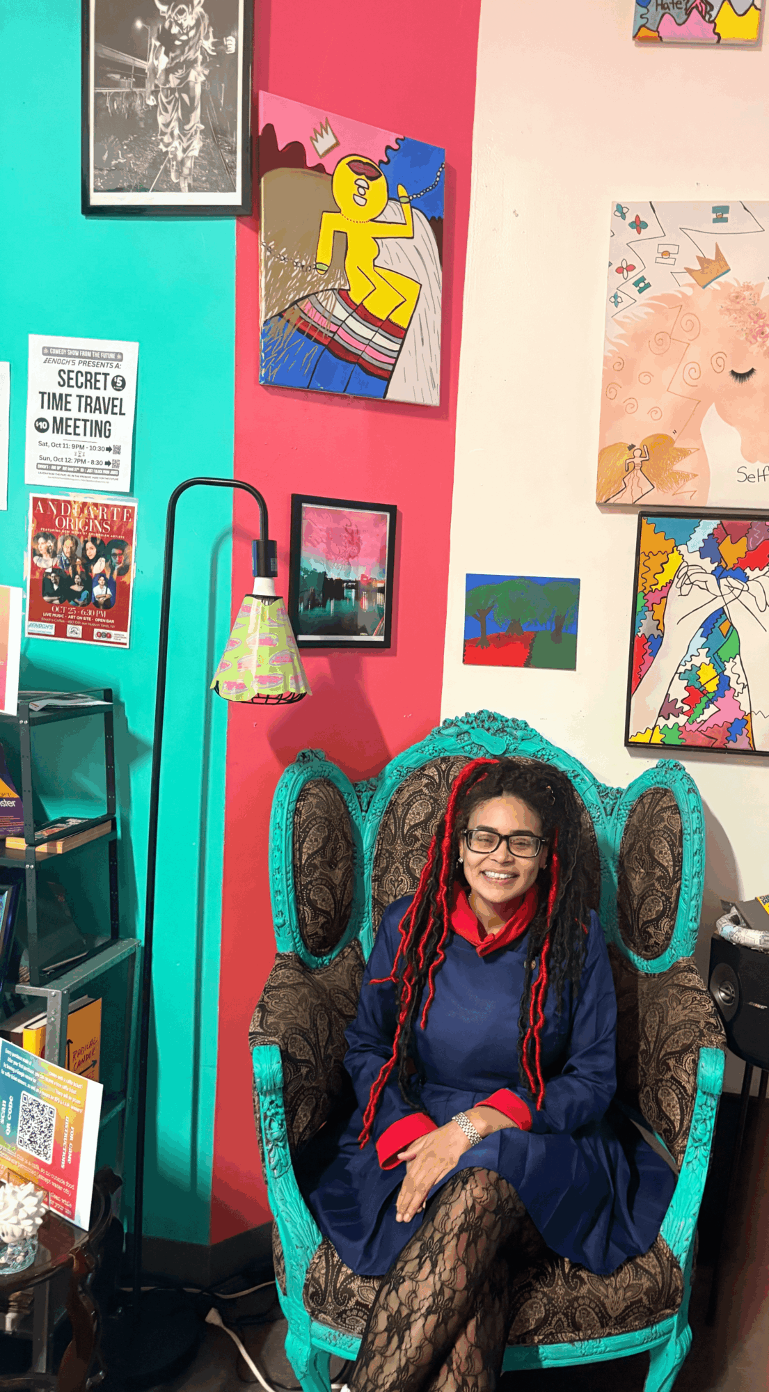 Girl with glasses and red braids sitting on a decorative chair in an art-filled room with colorful paintings on the wall.