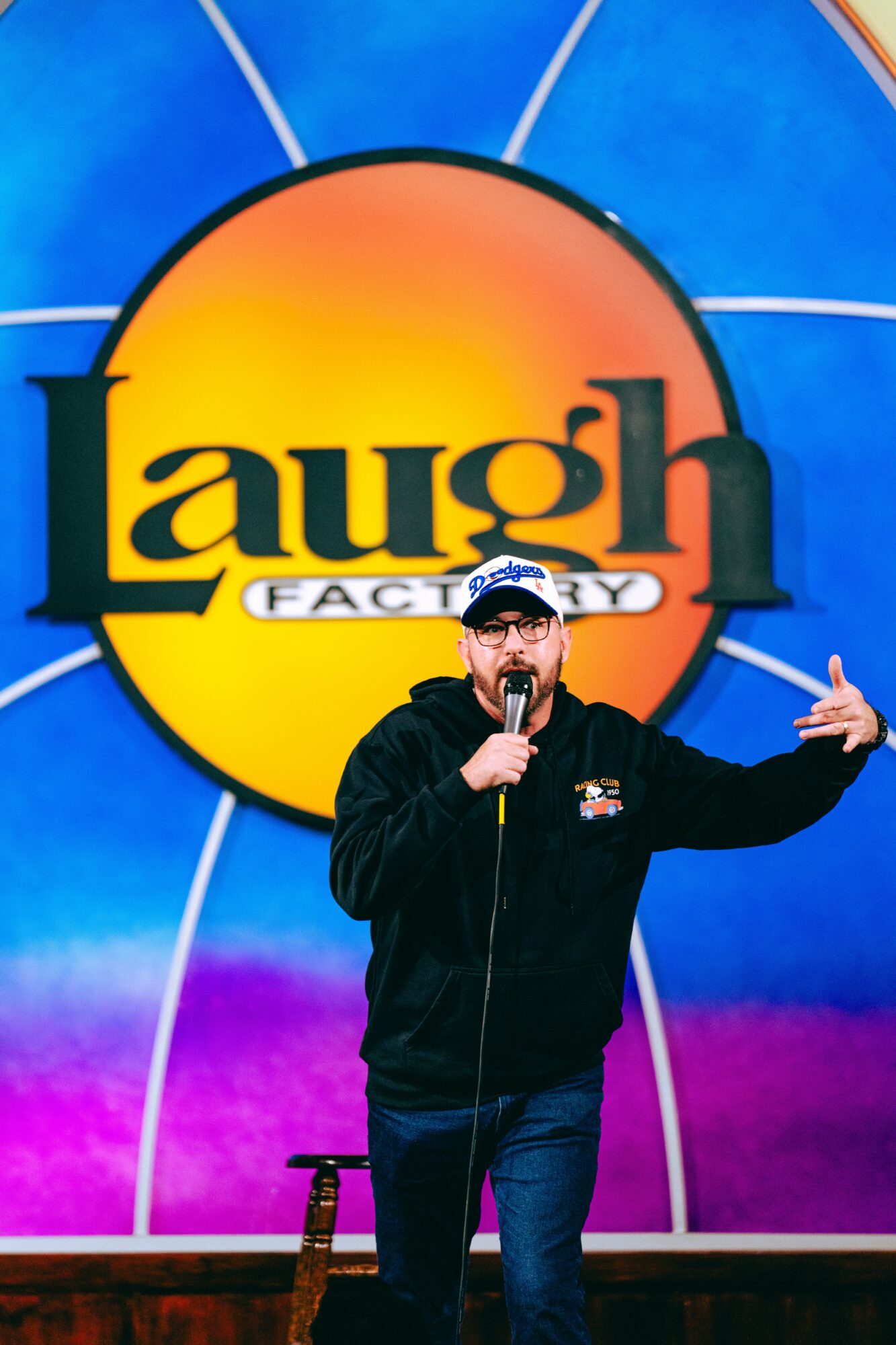 Person performing stand-up comedy on stage with a large Laugh Factory logo behind them.
