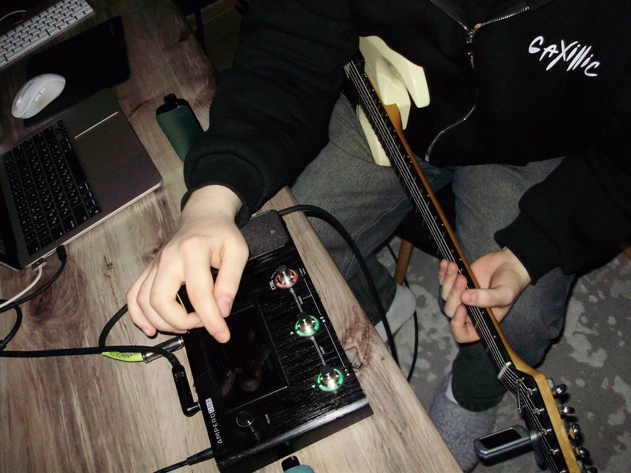 Person adjusting a black electronic device with green lights, sitting at a desk with a keyboard and other items nearby.