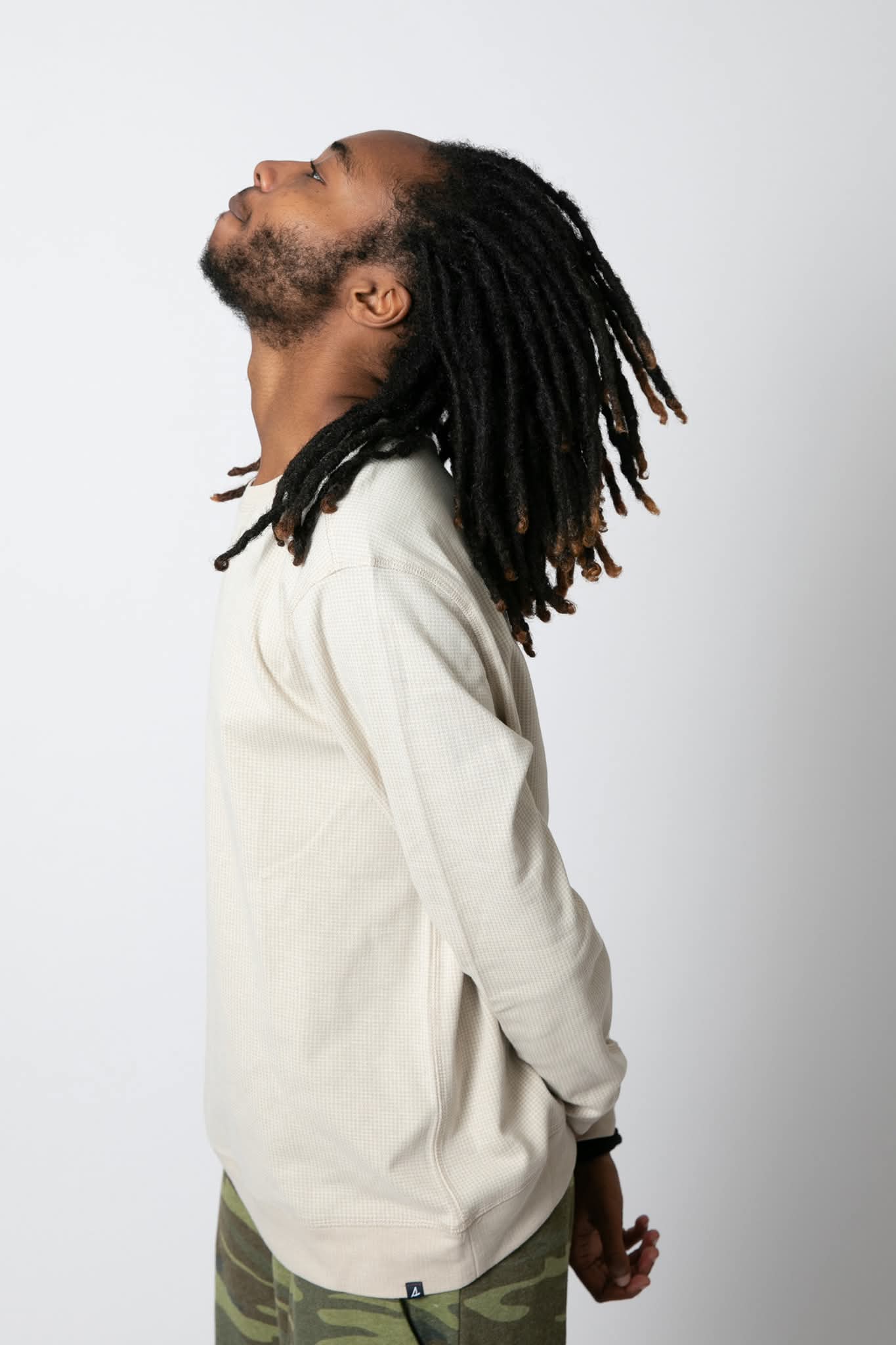 Side view of a man with dreadlocks wearing a light-colored shirt against a plain background.