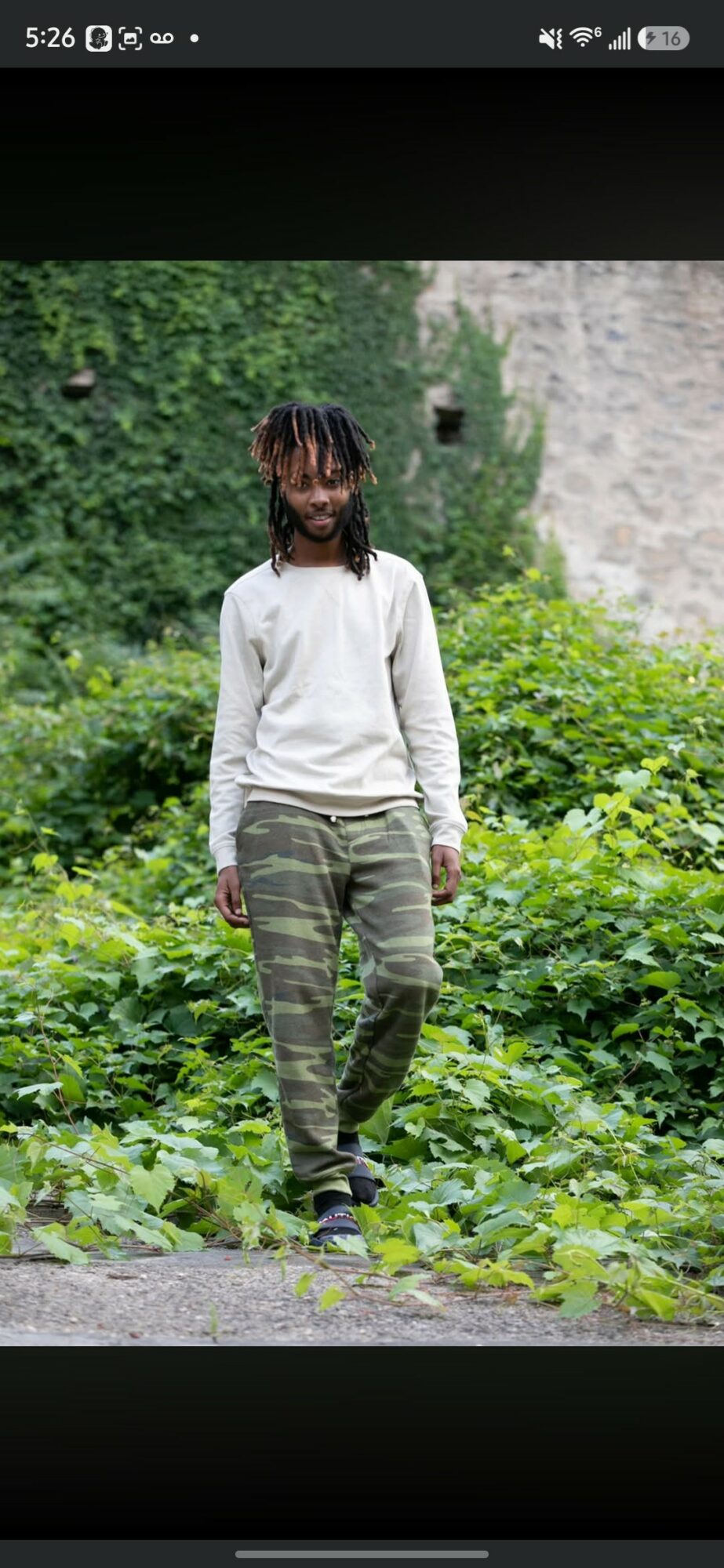 Person walking outdoors on a path with greenery and a stone wall in the background.