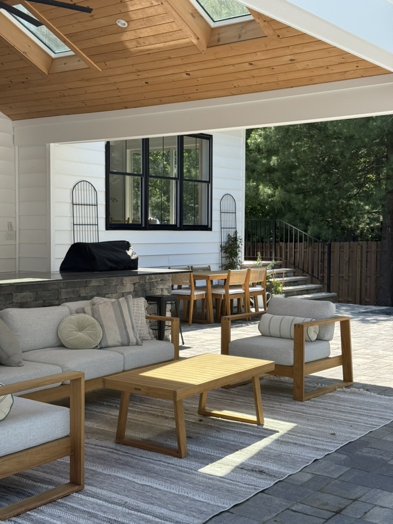 Living room with wooden ceiling, large window, outdoor view, and furniture including sofas, chairs, and a wooden table.