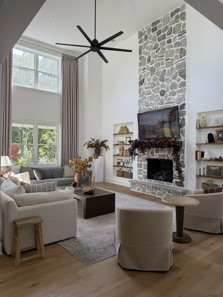 Living room with high ceiling, stone fireplace, large window, and modern furniture, including a sofa, armchair, and coffee table.