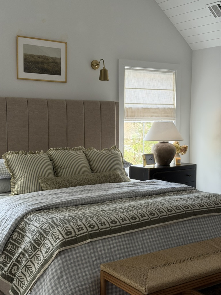 Bedroom with a bed, pillows, a nightstand with a lamp, window, and wall art, in a bright room with a sloped ceiling.
