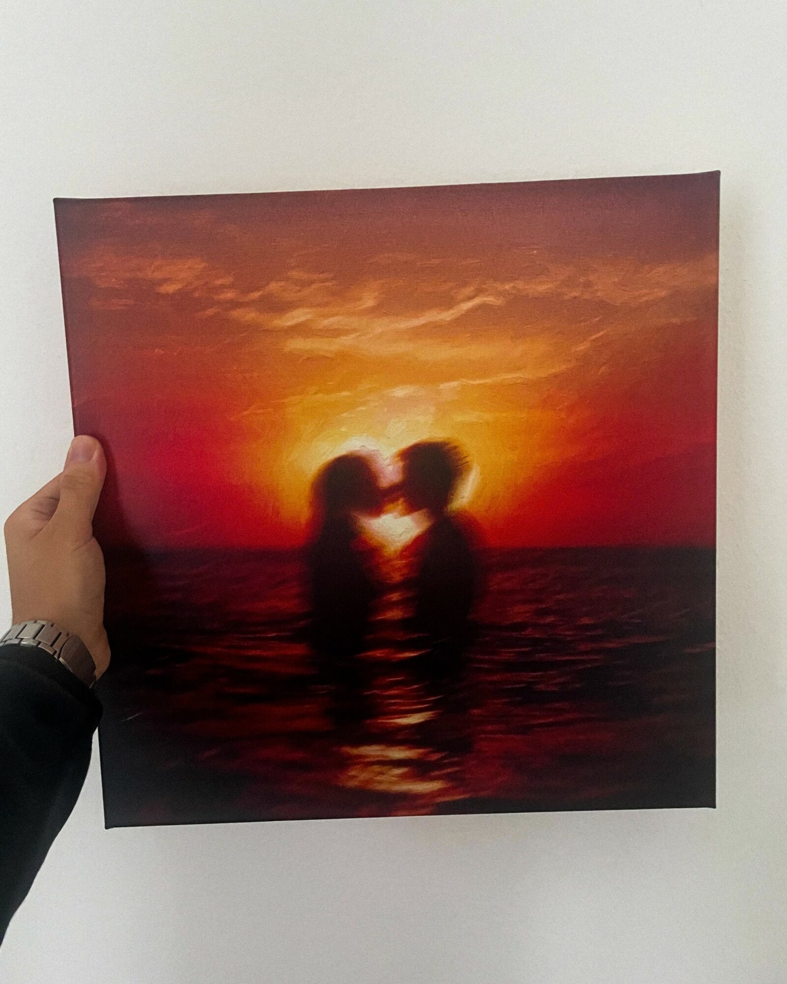 Person holding a photo of two people kissing at sunset over water, with a vibrant orange sky.