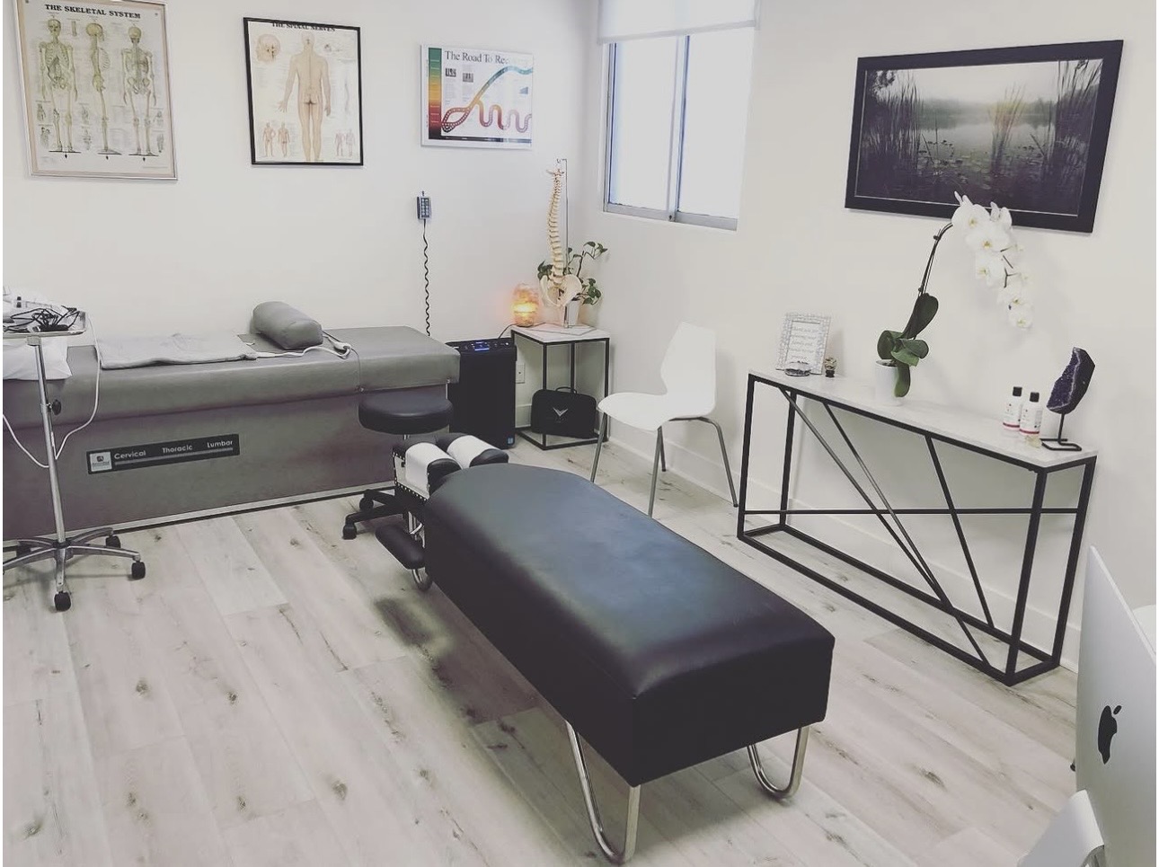 Medical examination room with a bed, chair, and medical equipment, bright and clean with white walls and light flooring.