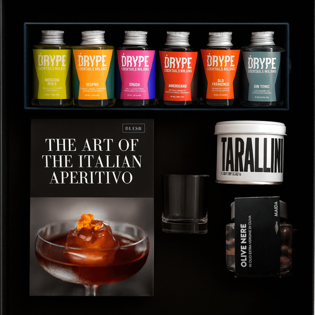 Six colorful bottles of DRYPE supplements, a Tarallini container, a black glass, a book titled 'The Art of the Italian Aperitivo', and a jar of olive tapenade on a black shelf.