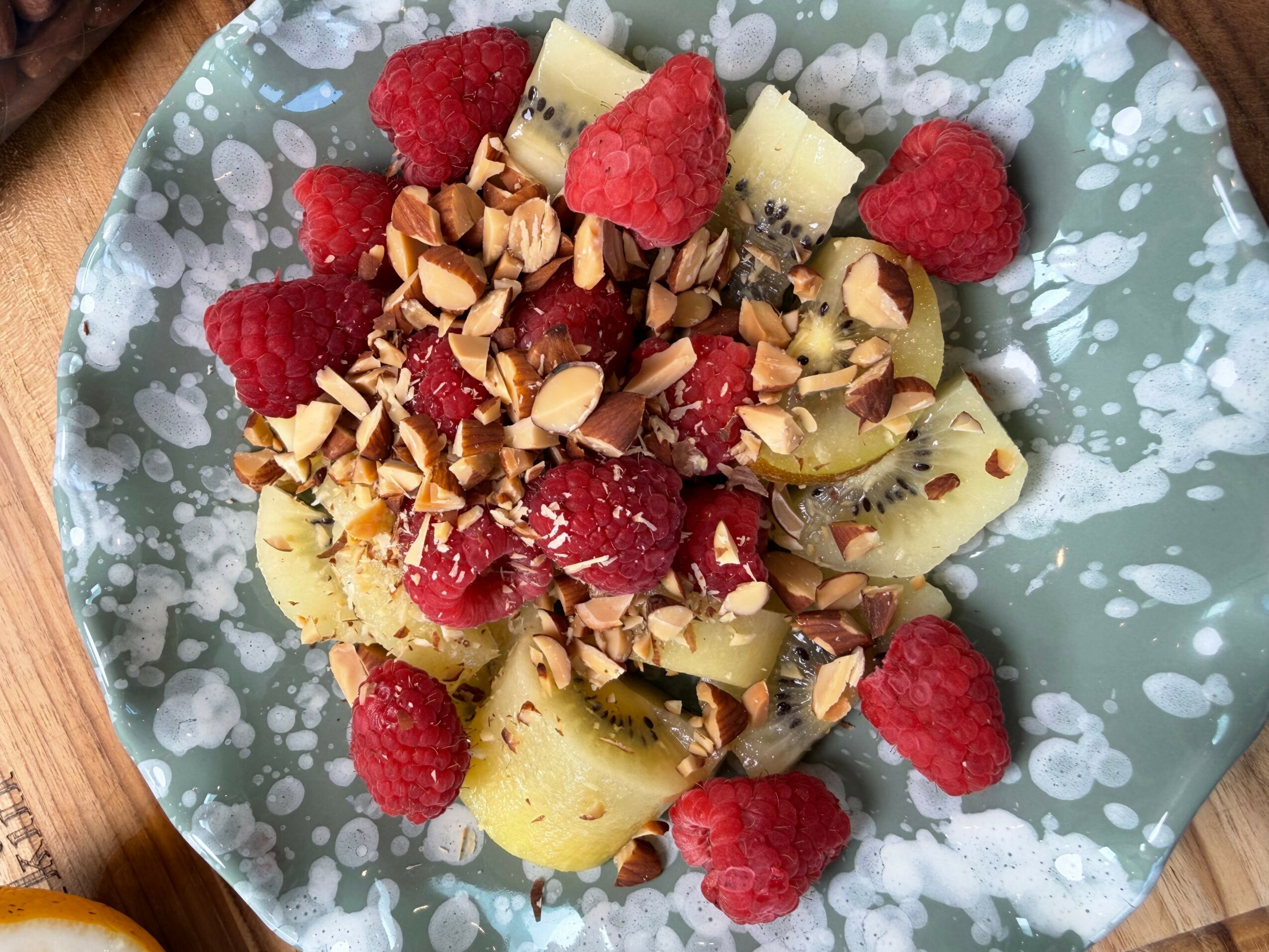 Fruit salad with bananas, raspberries, sliced kiwi, topped with chopped nuts on a blue patterned plate