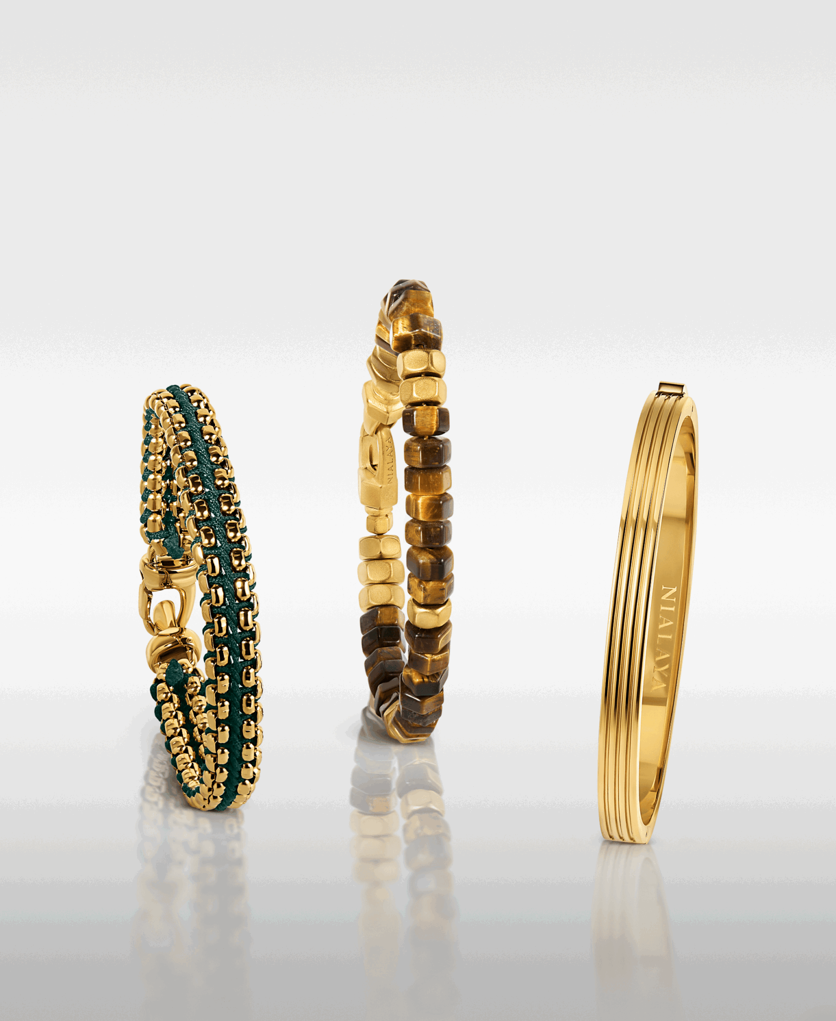 Three gold rings with different designs, one with green and black beads, one with small square beads, and one plain with engraved text.