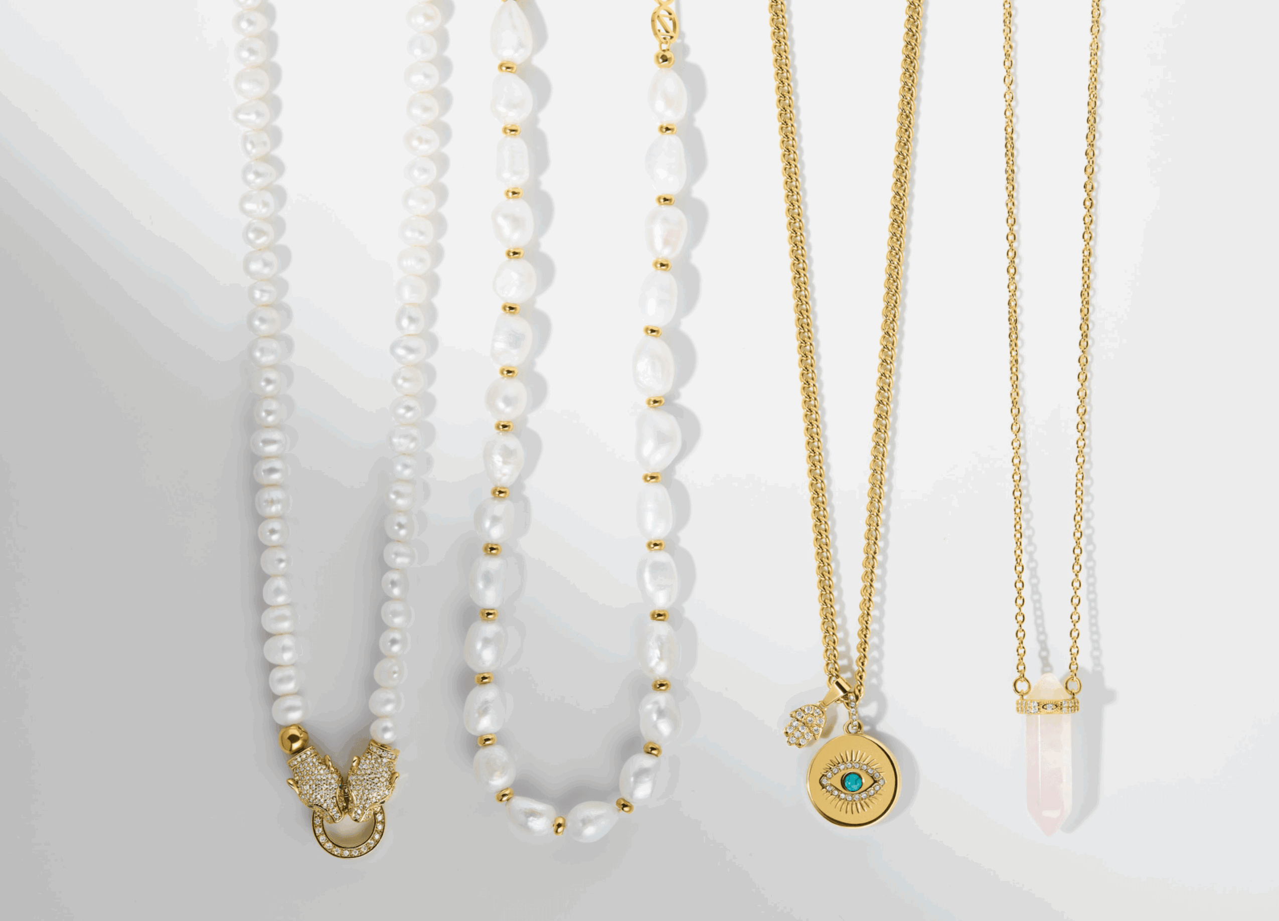 Five necklaces hanging, with pearls, gold chains, and a pendant with an eye design, against a white background.