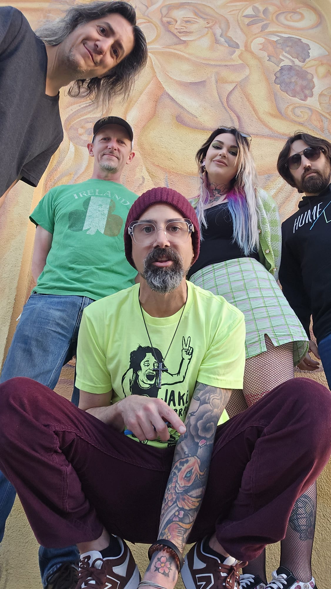 Group of five people outdoors, with a mural in the background, smiling and posing for the photo.