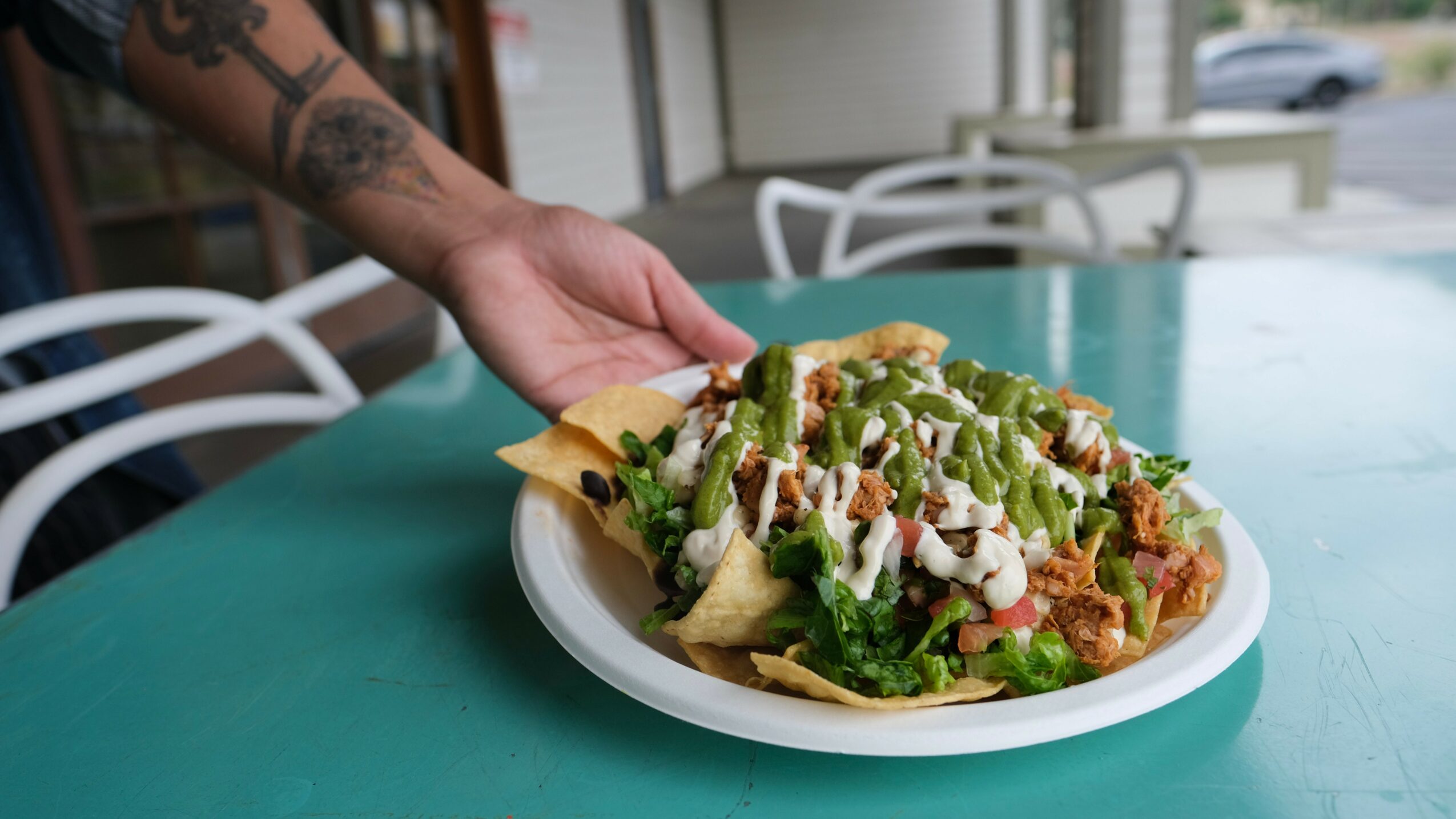 Hand placing a taco on a plate filled with lettuce, cheese, and meat, on a turquoise table.