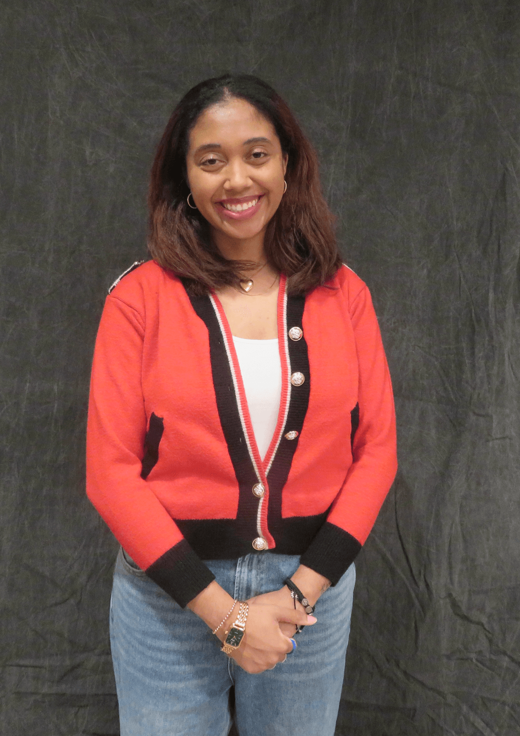 Young woman with shoulder-length hair smiling, wearing a red jacket with black and white accents, and blue jeans.