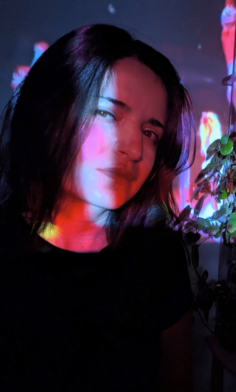 Young woman with dark hair in a dark room with colorful light reflections, looking at the camera.