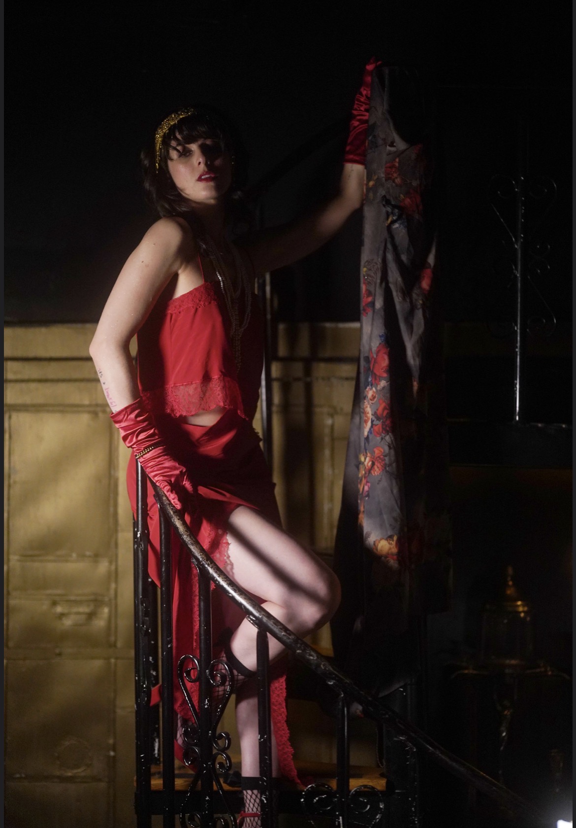 Woman in red dress and gloves holding a colorful fabric, standing near a railing at night.