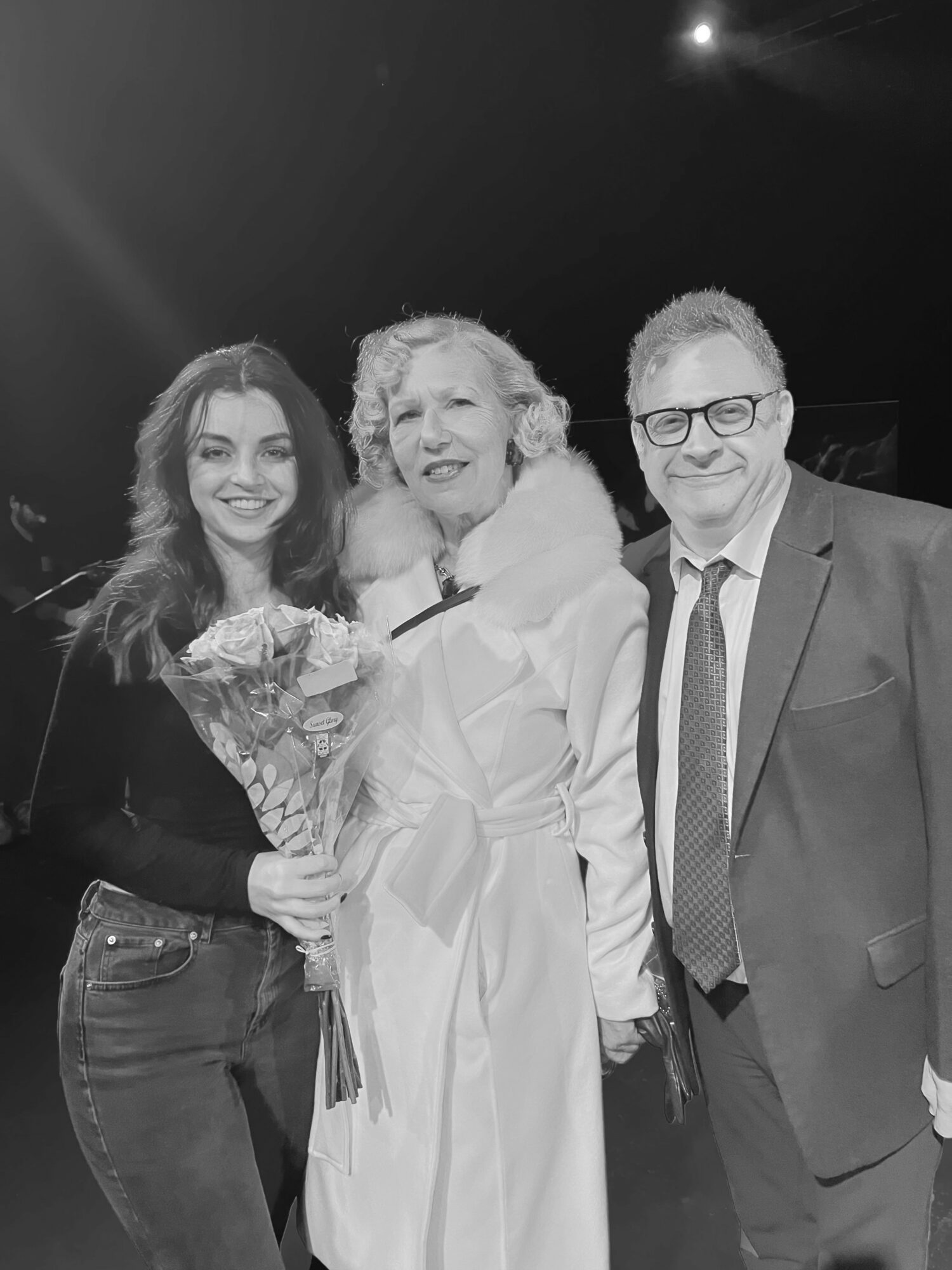 Three people smiling, two women and one man, standing together in formal attire, with a dark background.