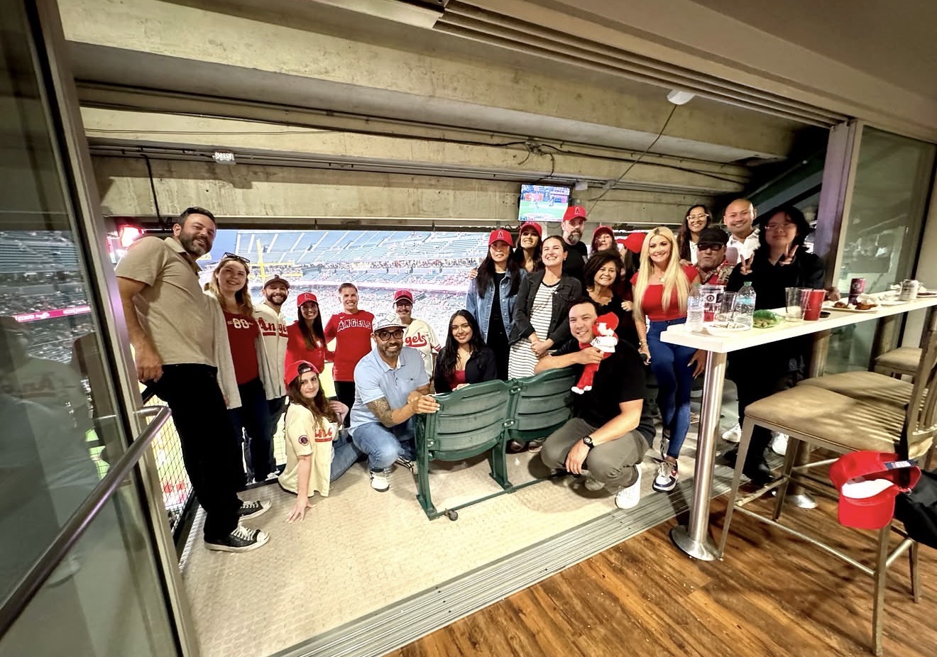 Group of people gathered indoors near a window, some sitting on a bench, others standing, with a view outside.