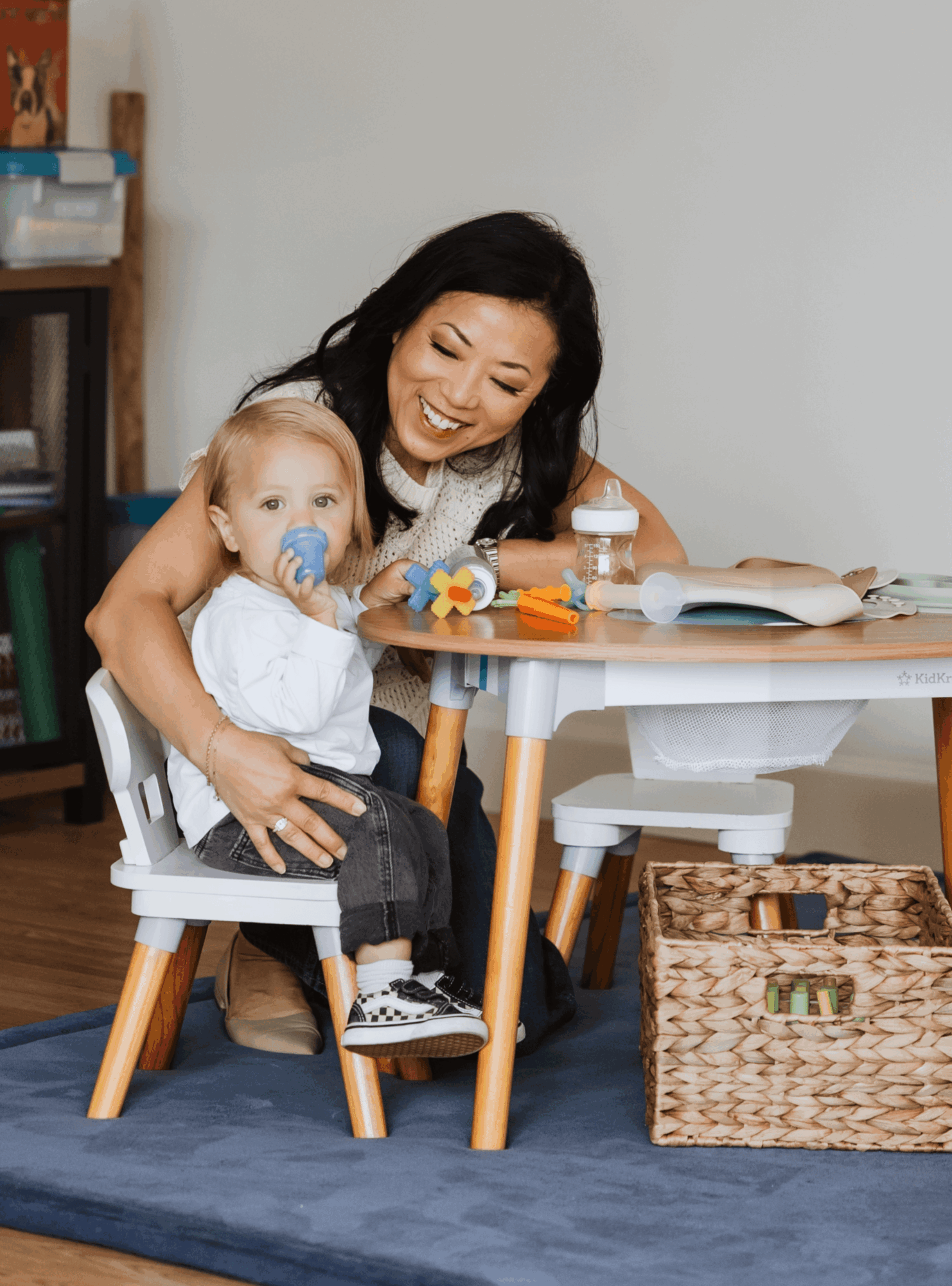 Woman and young girl sitting at a table with toys and books, smiling and playing together.