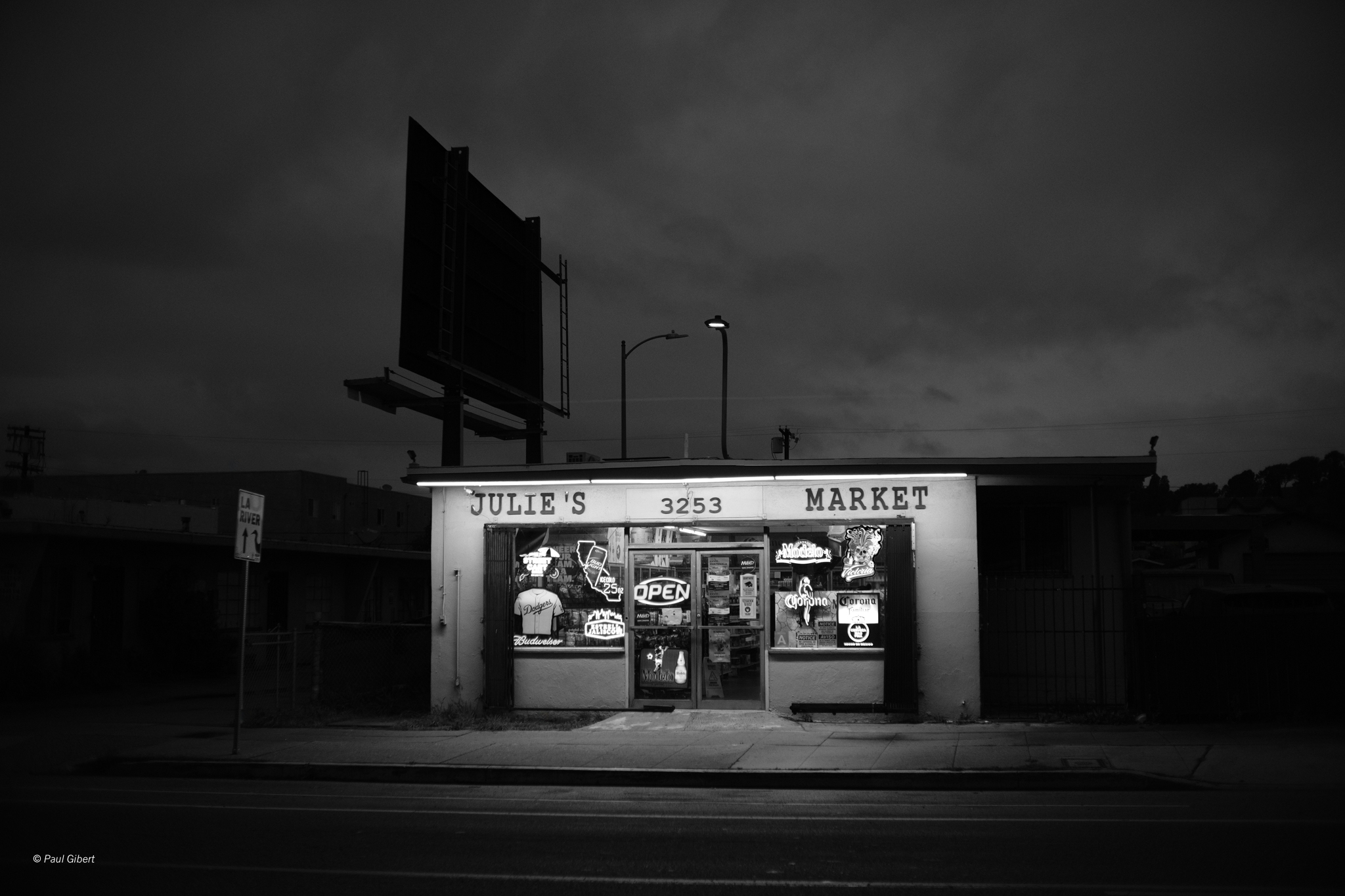 Small store with illuminated windows, sign reads 'Julie's Market,' dark cloudy sky, street in front.