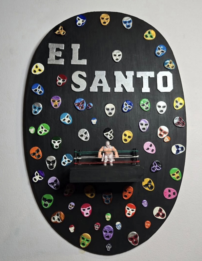 Oval display with masks and the words 'EL SANTO' above a small figure on a bench.