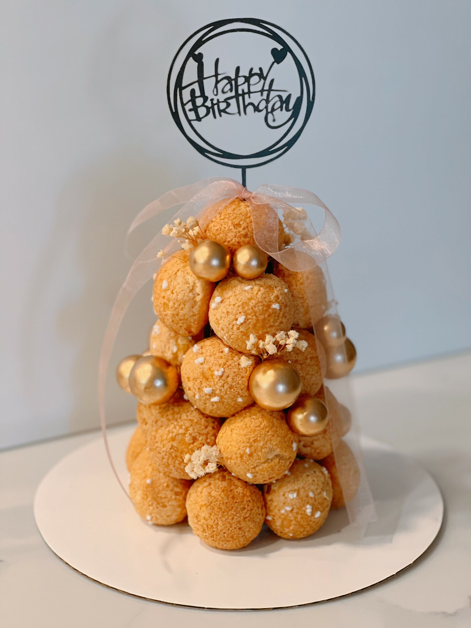 Small round cookies decorated with pearls and white sprinkles, arranged in a tree shape with a birthday topper, on a white surface.