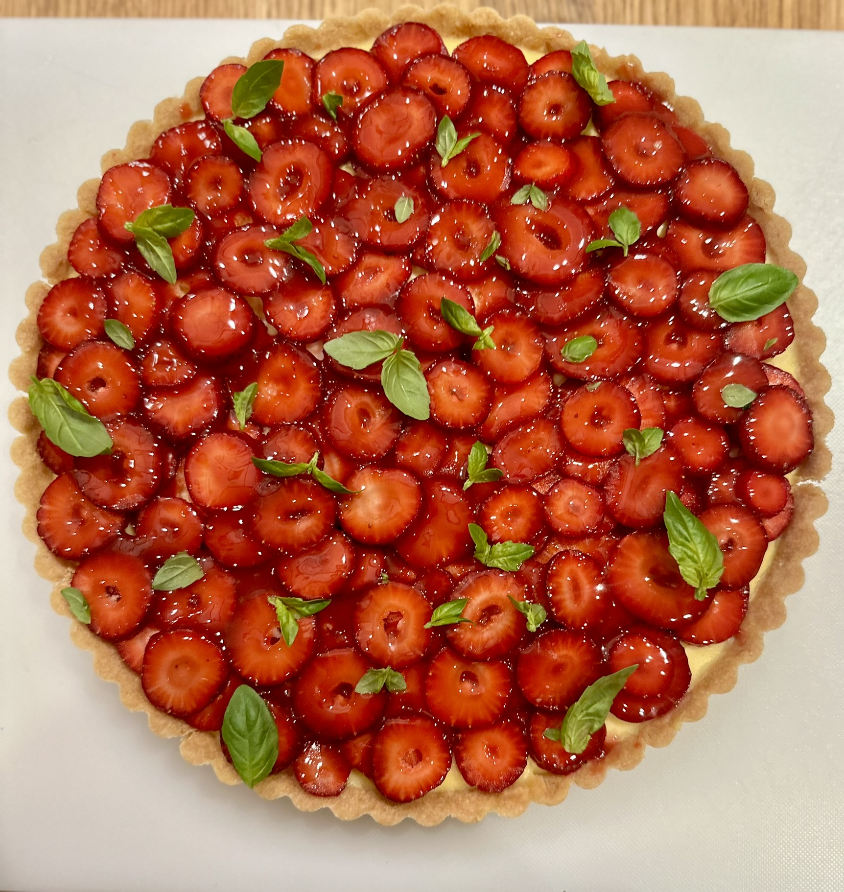 Heart-shaped tart topped with strawberries and green leaves on a white surface.
