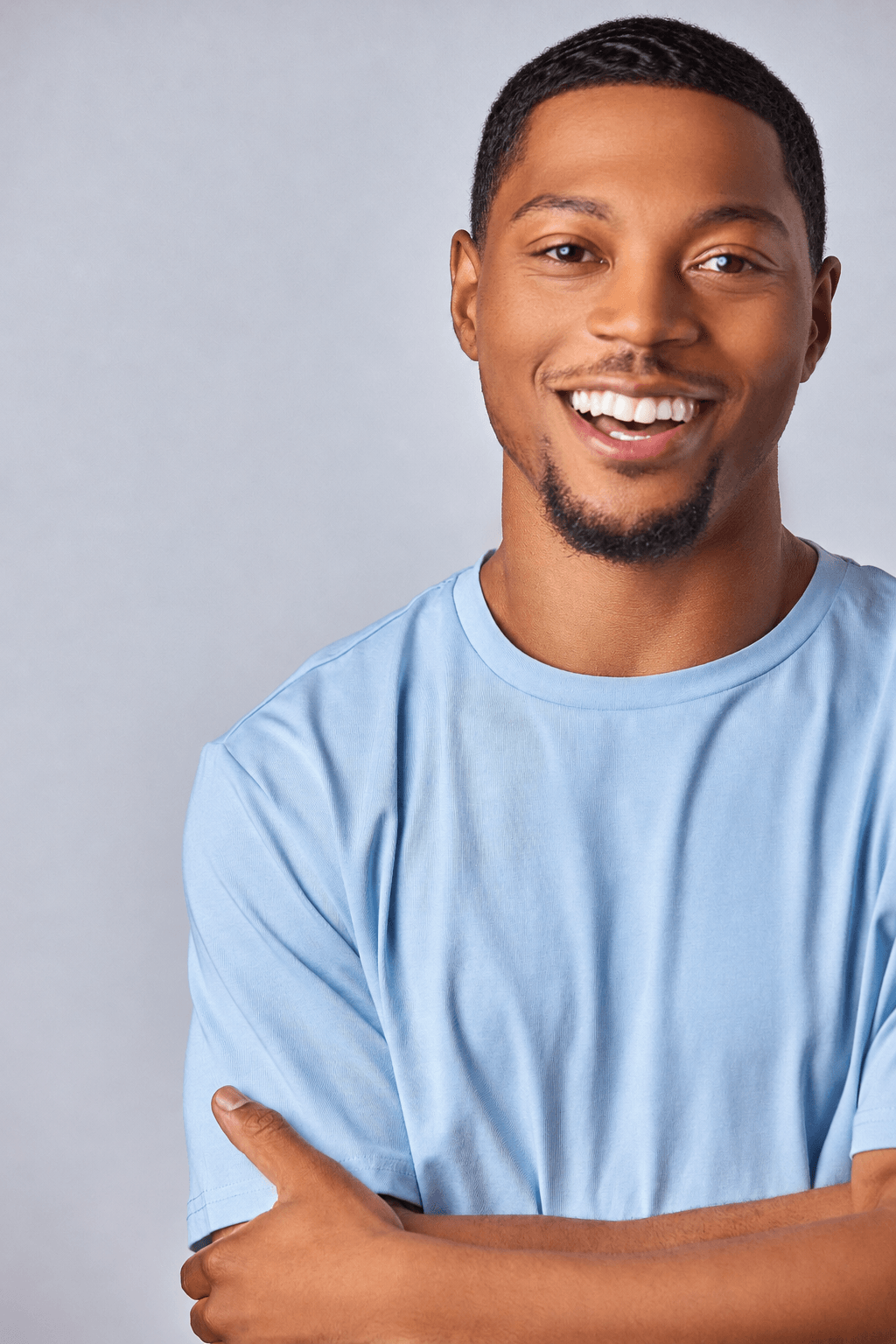 Smiling young man with short hair and a goatee, wearing a light blue shirt, standing against a plain background.
