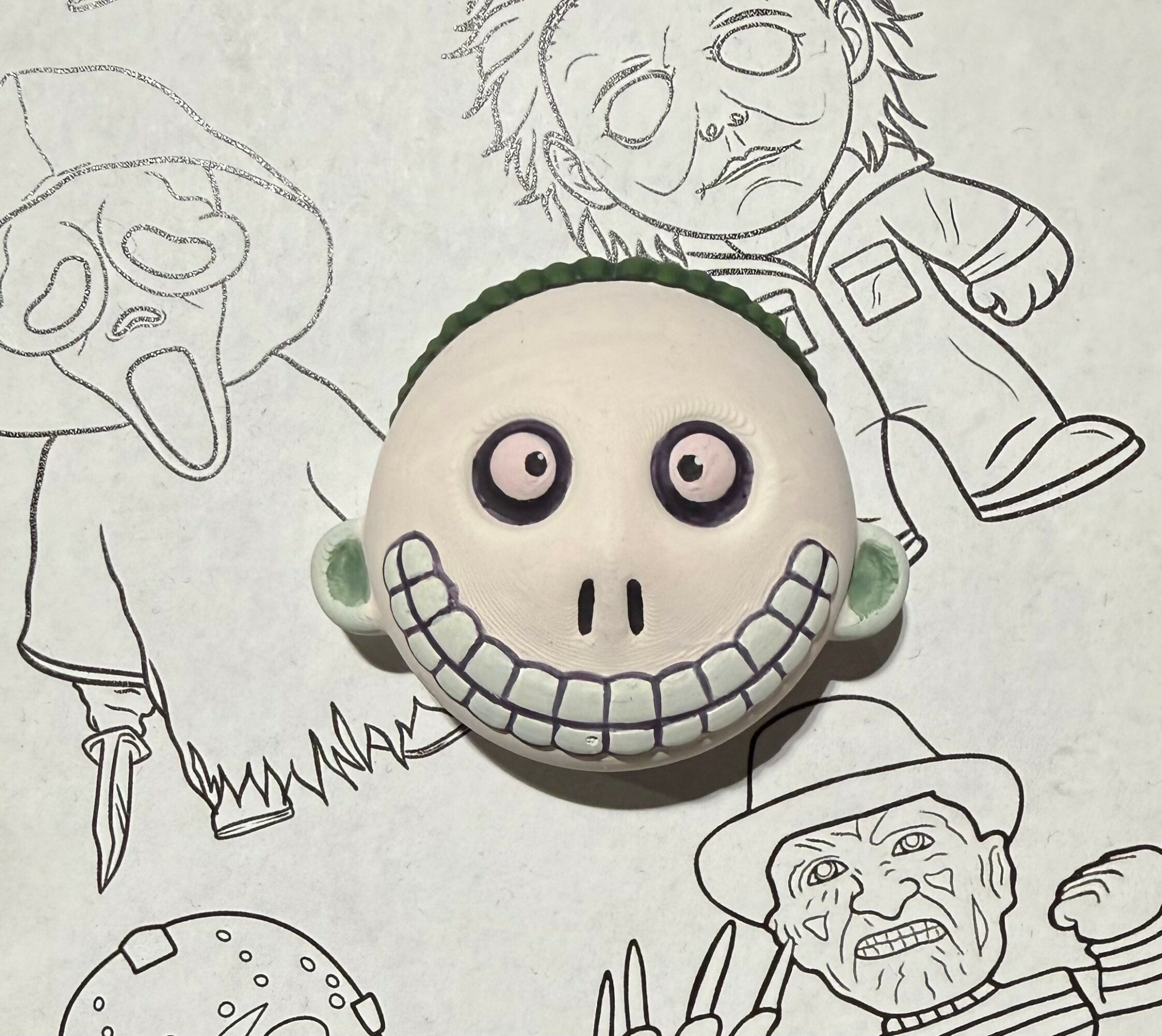 A plush skull with large eyes and a wide, toothy grin placed on a background of hand-drawn cartoon characters.