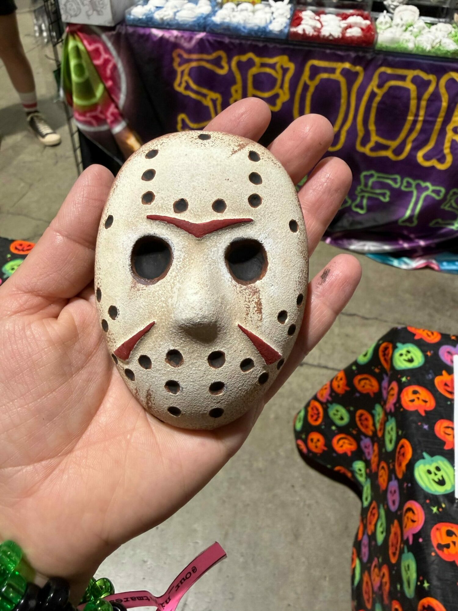 Person holding a small, white, hockey mask-shaped object with holes and black eye openings.