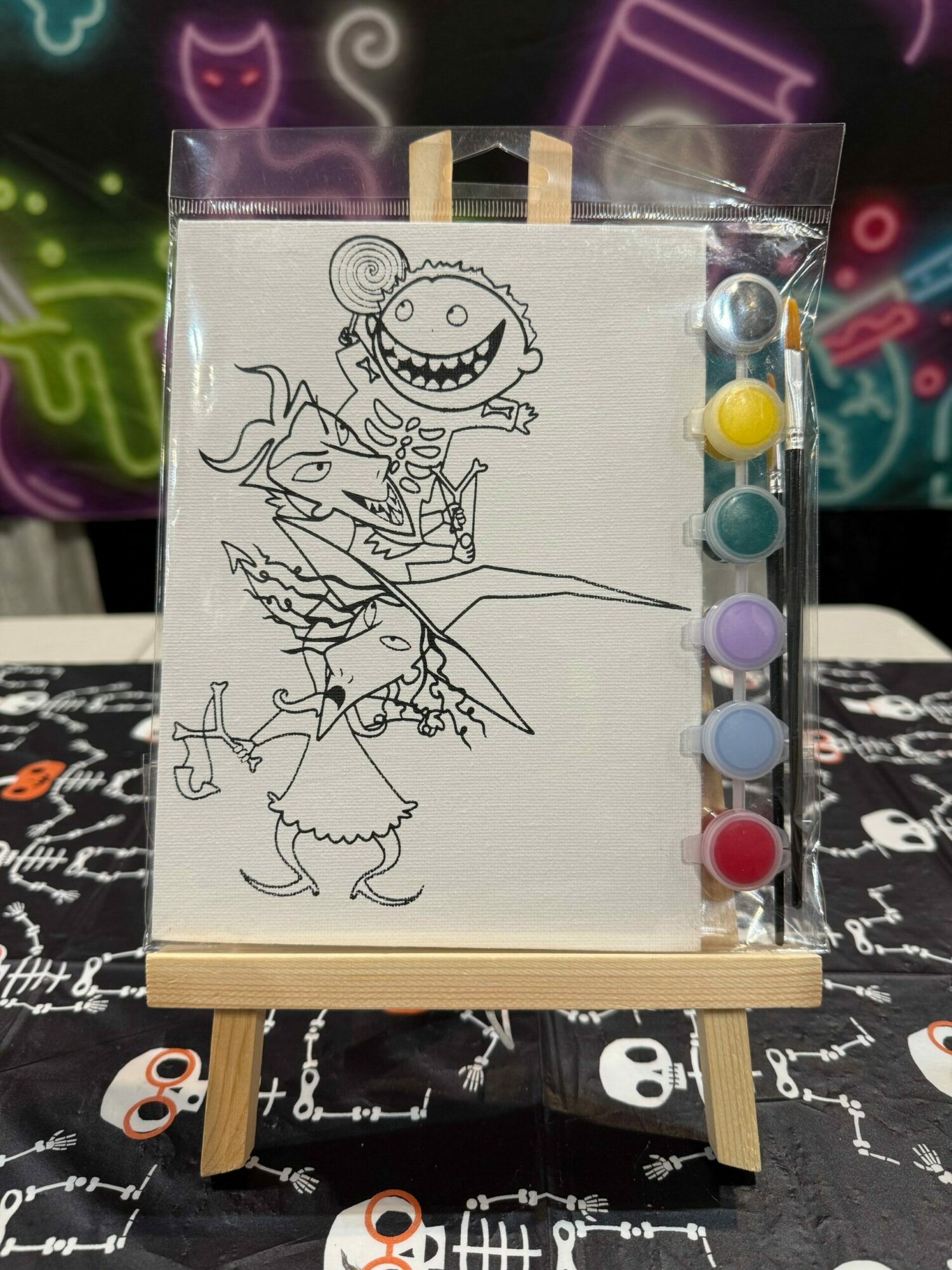 Line drawing of a unicorn and a dragon on paper, with colorful pins at the top, displayed on a wooden stand.