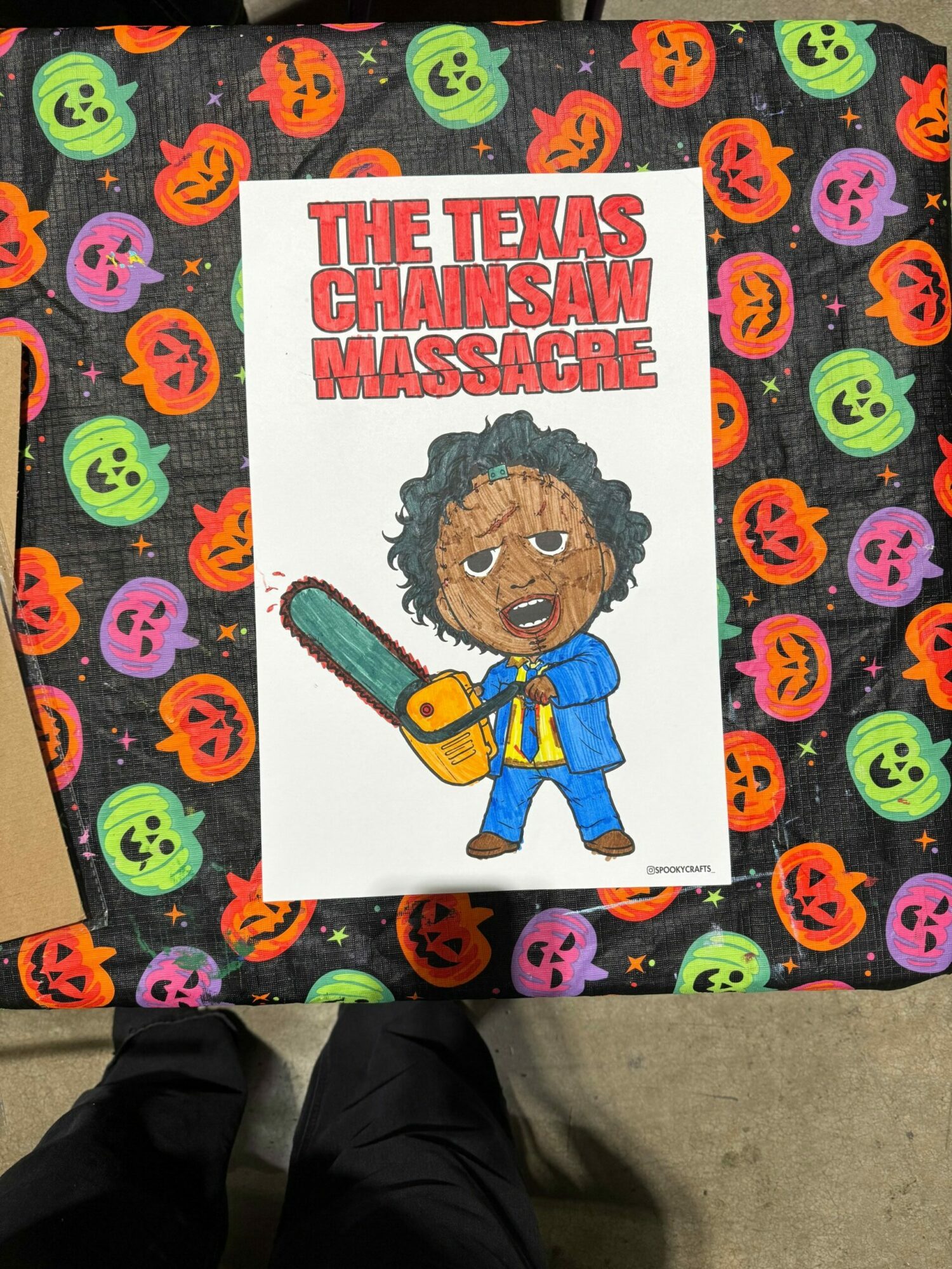 Book cover titled 'The Itsy Bitsy Mummy and the Mummy's Curse' with a cartoon character holding a chainsaw, on a Halloween-themed tablecloth.