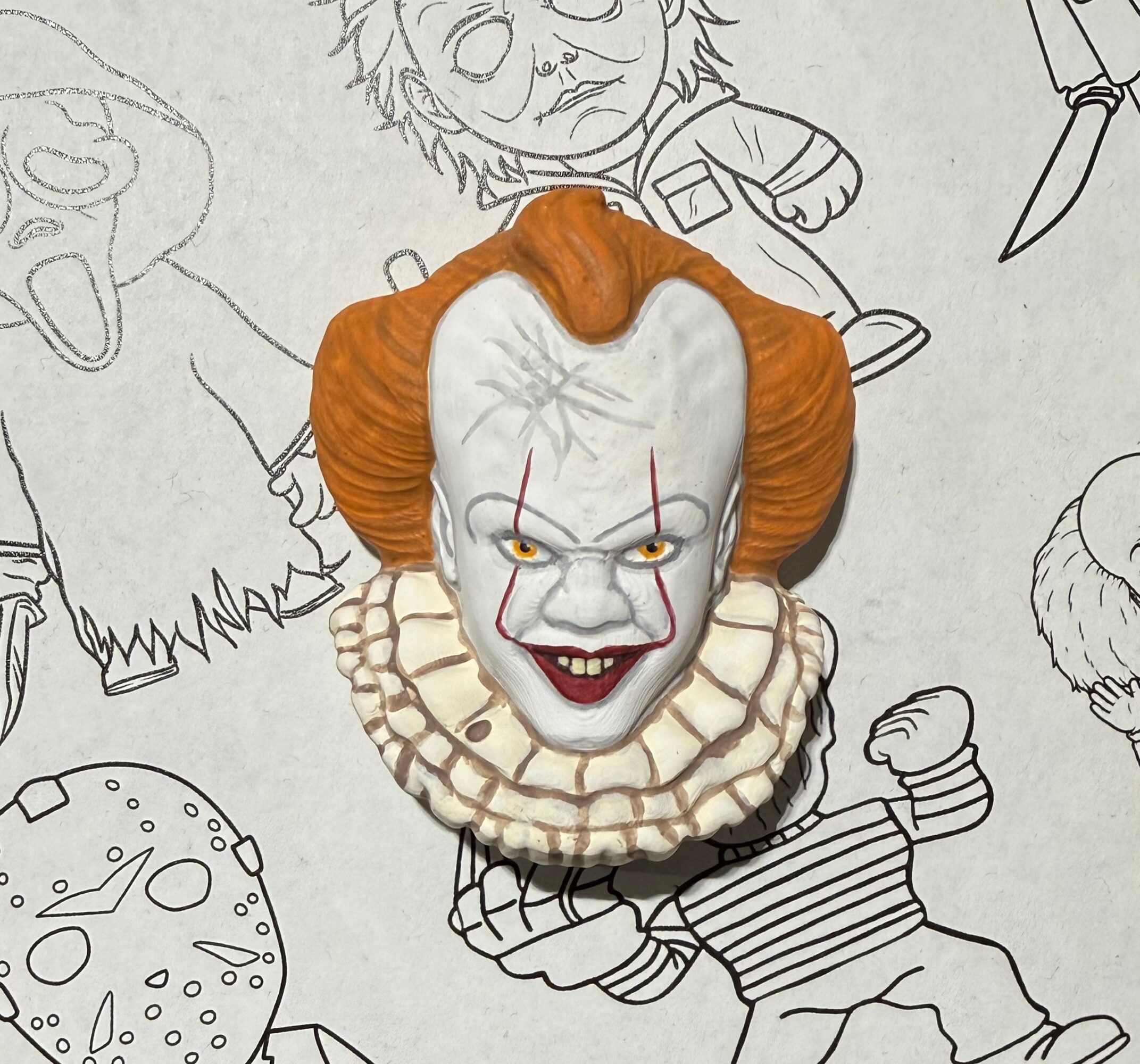 Clown figurine with orange hair, white face, and ruffled collar, placed on a sketch of a cartoon character.