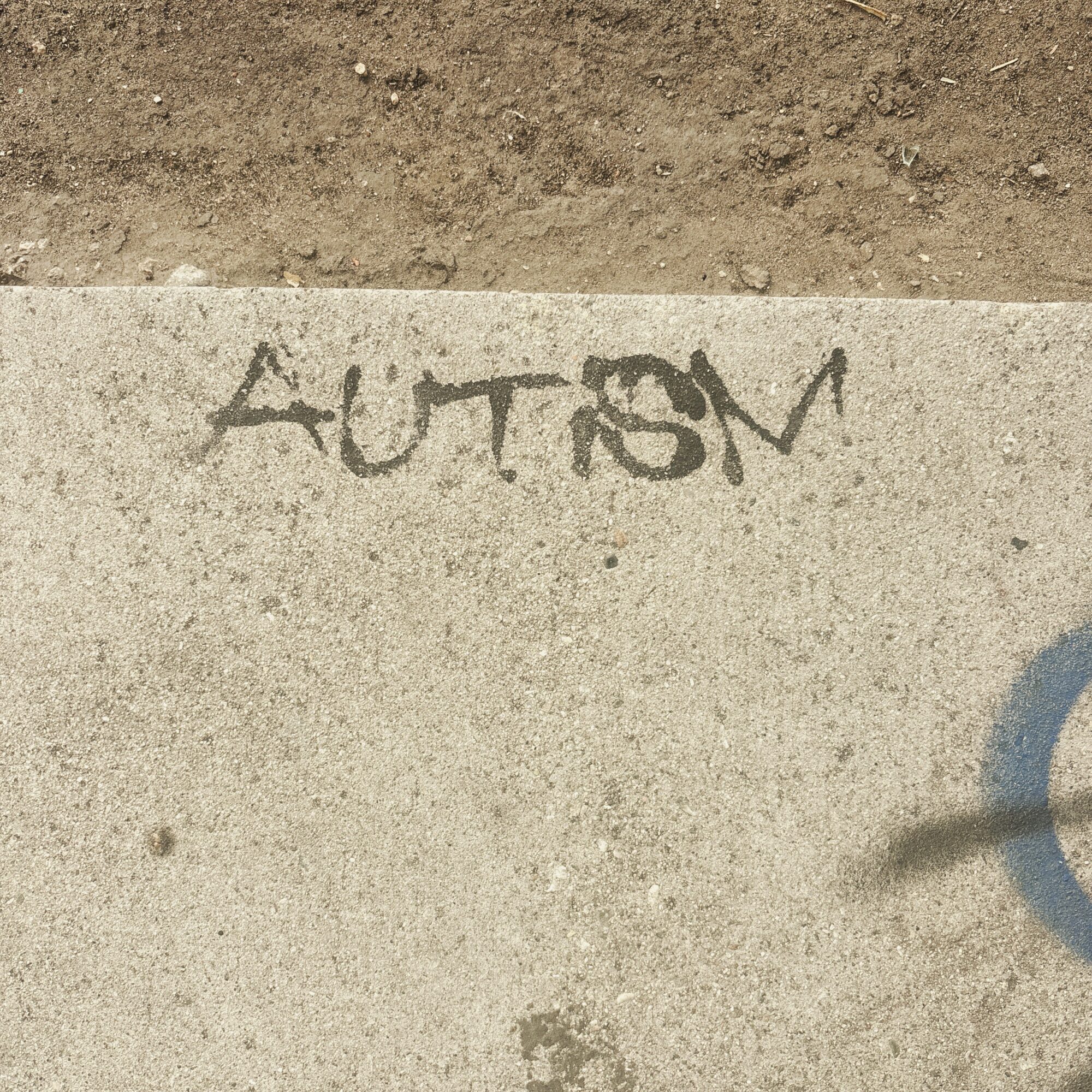 Graffiti on concrete sidewalk with dirt above, partially visible blue circle on right side.