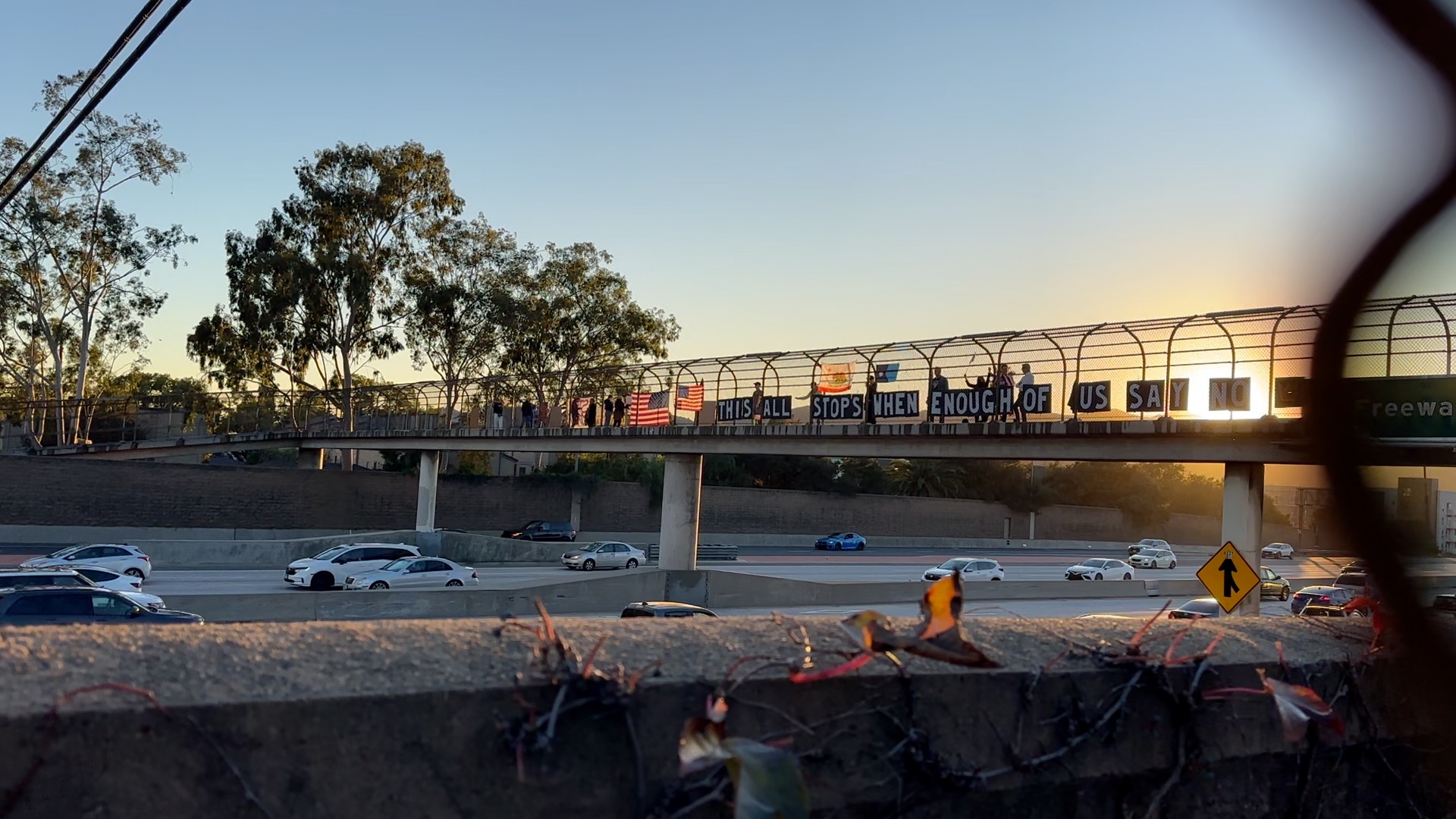 Bridge with pedestrians and cars, trees in background, sunset sky, and construction debris in foreground.