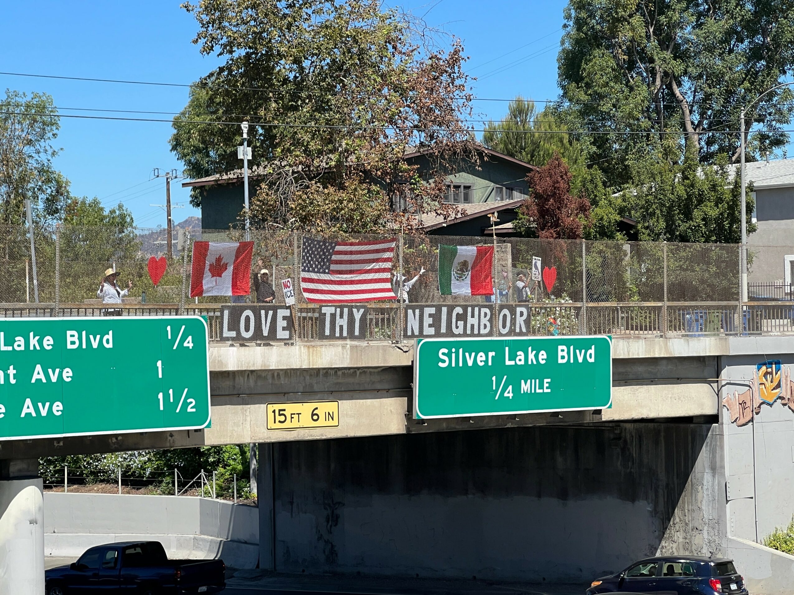 Bridge with signs and flags, trees, and a clear blue sky in the background.