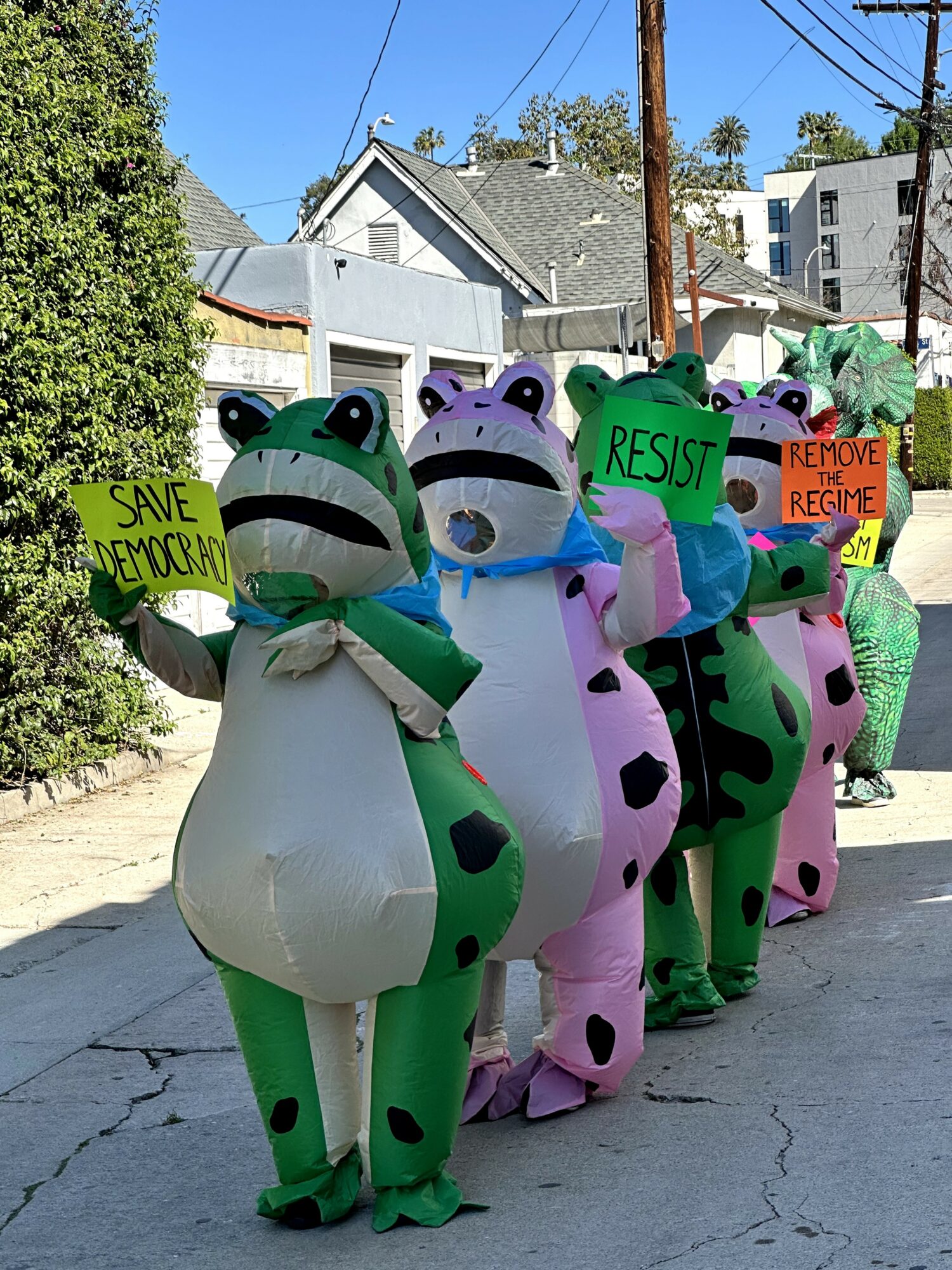 Group of people in colorful animal costumes holding protest signs, standing outdoors on a sunny day.