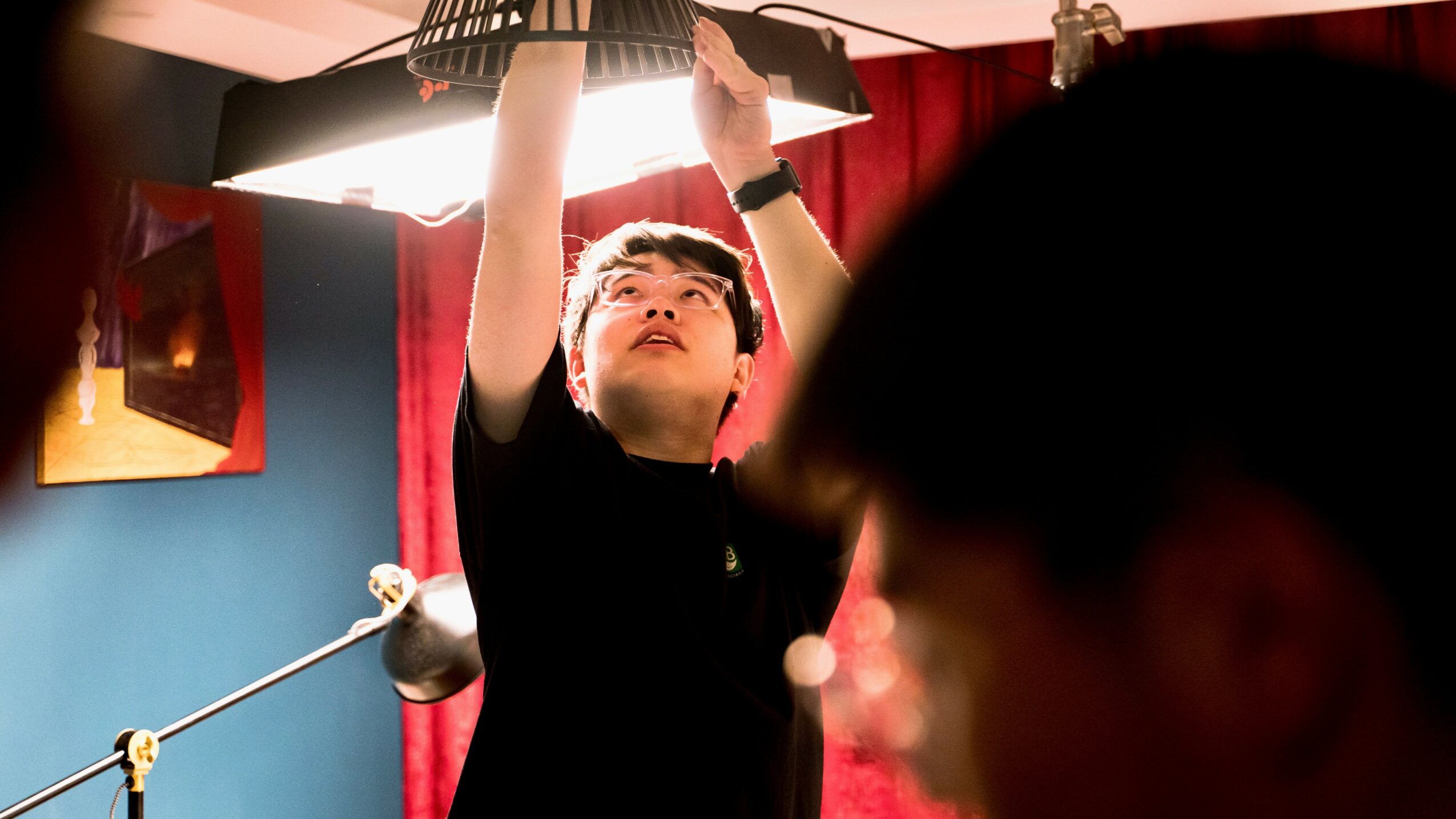 Person adjusting a ceiling light fixture in a room with red curtains and blue walls.
