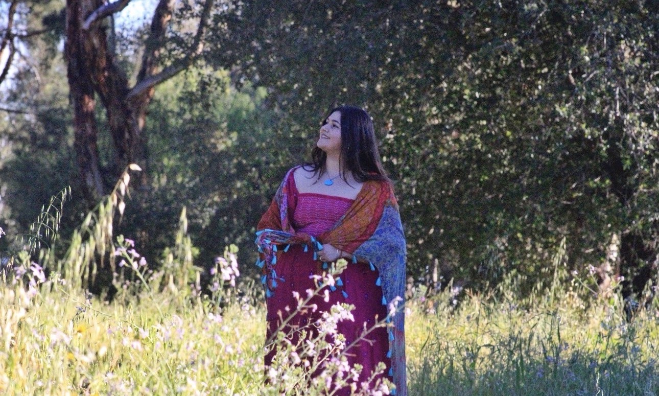 Woman in colorful dress standing in a grassy field with trees in the background.