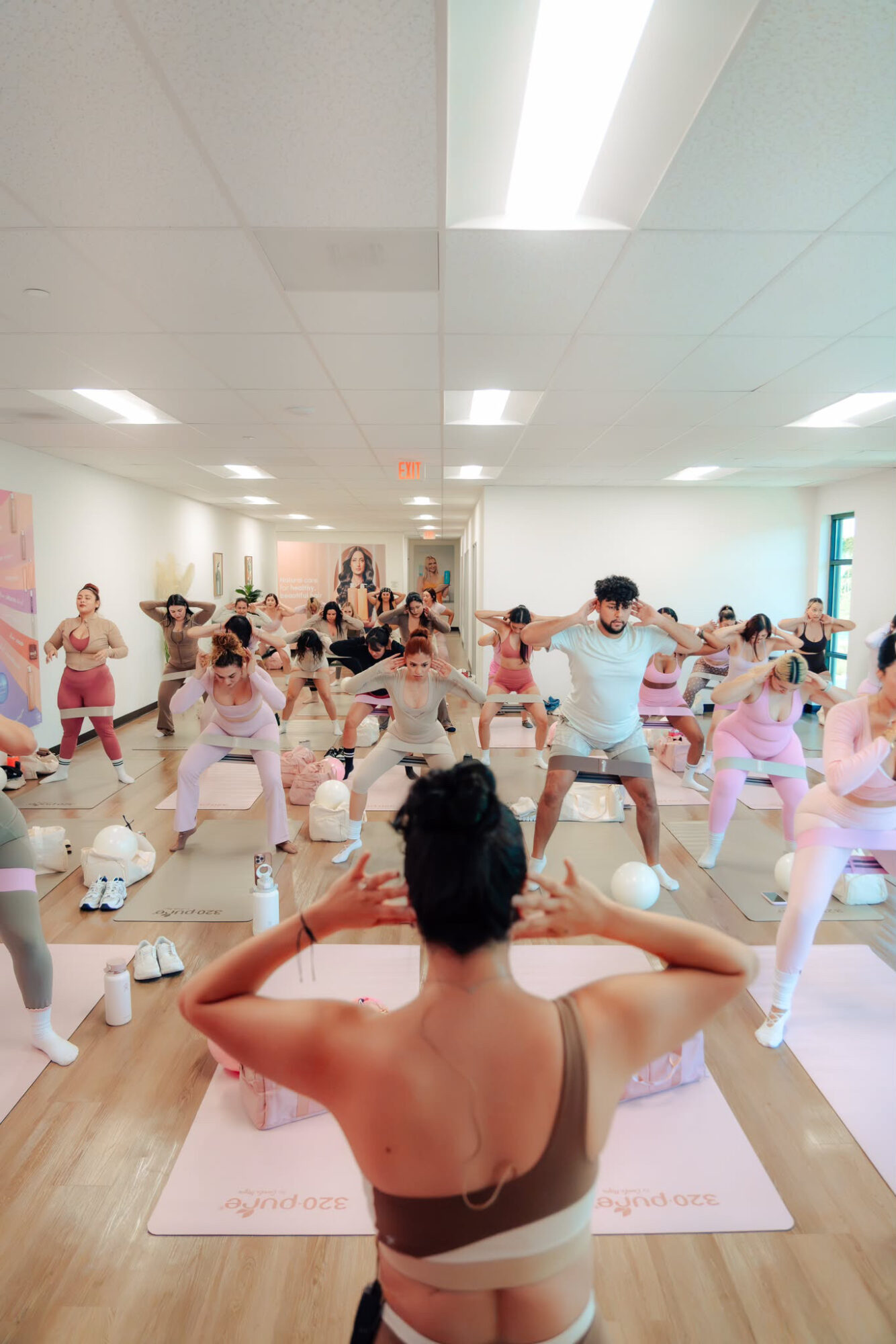 Group of people participating in a fitness class in a bright room, viewed from the instructor's perspective, with arms raised.