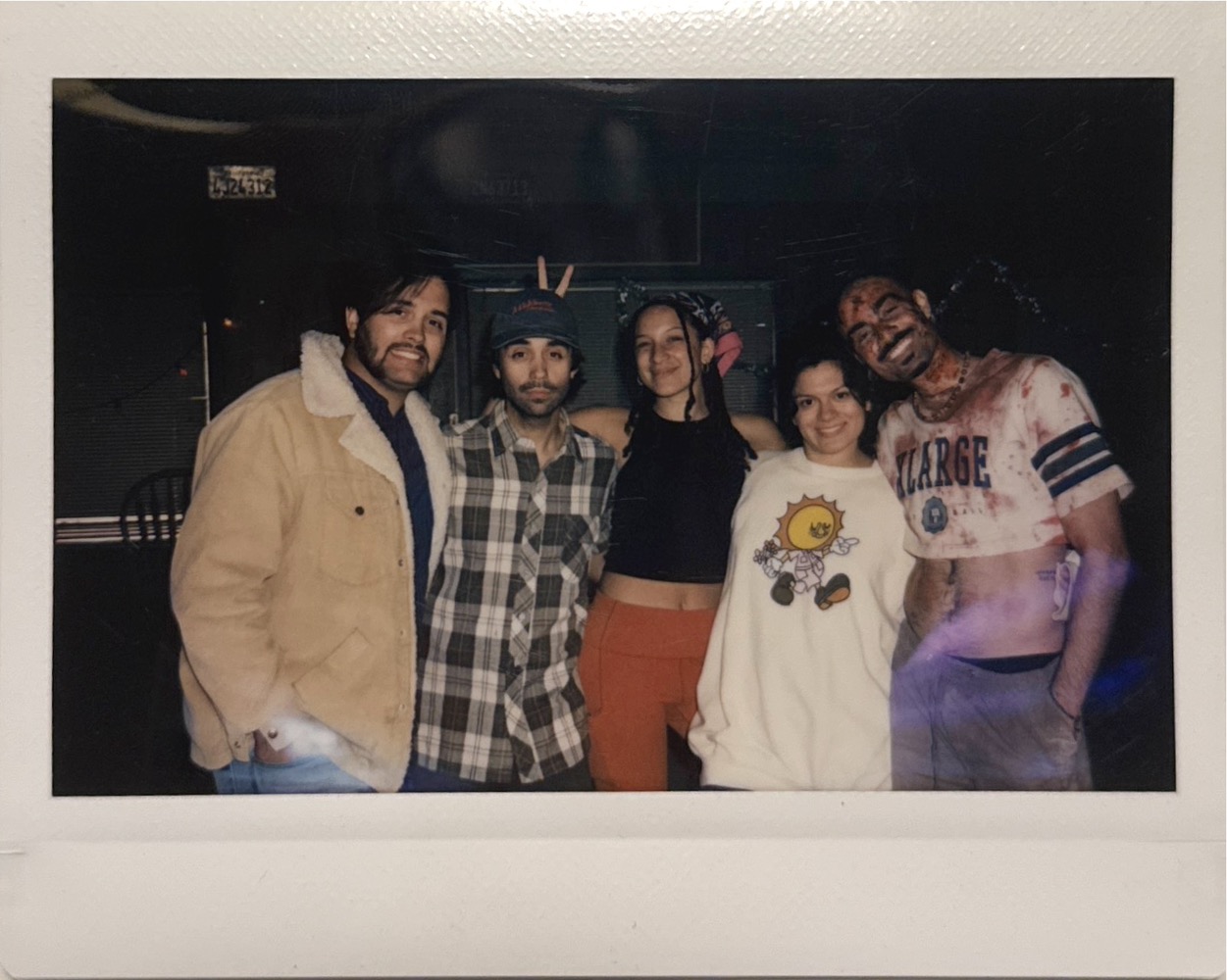 Group of five people standing together indoors, smiling, with dark background and some lighting effects.