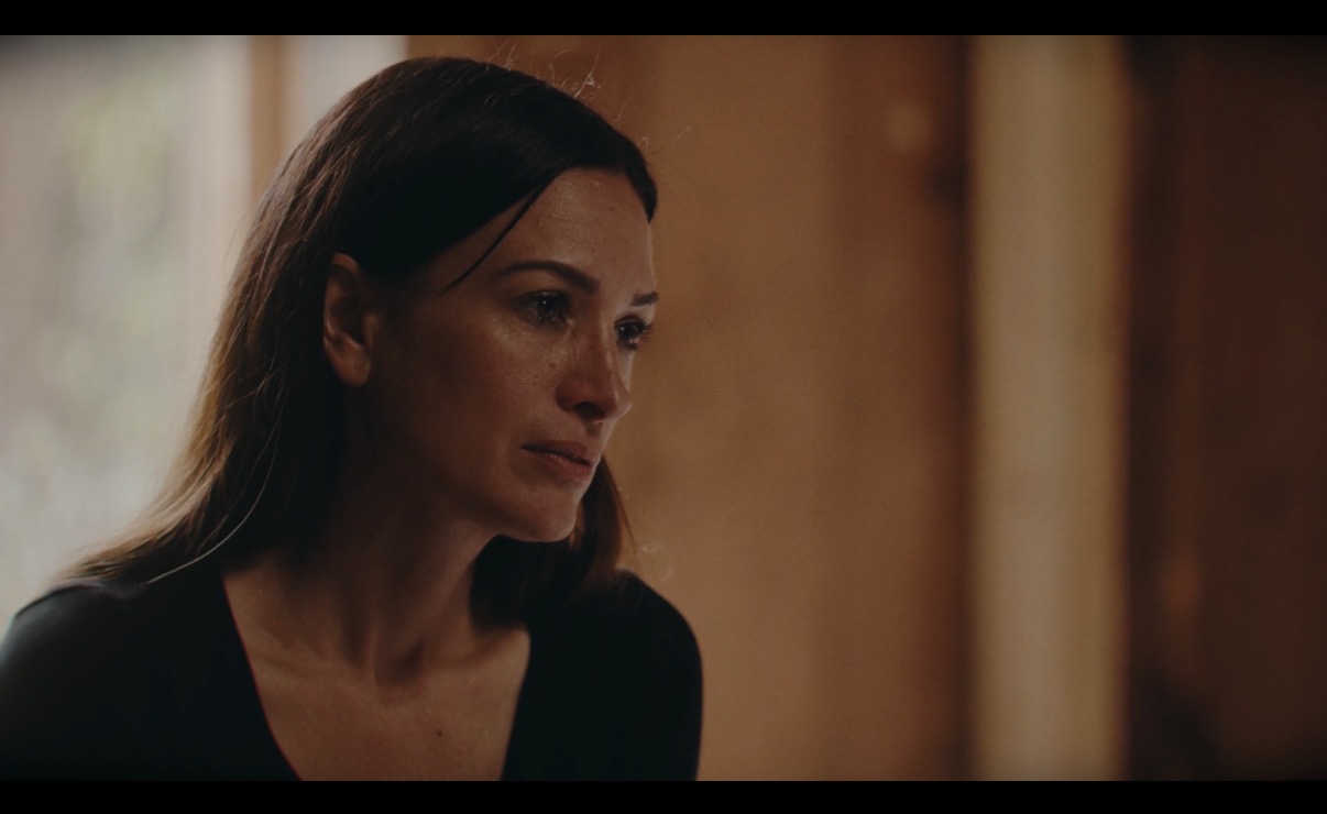 Woman with dark hair looking to the side in a dimly lit room with wooden walls.