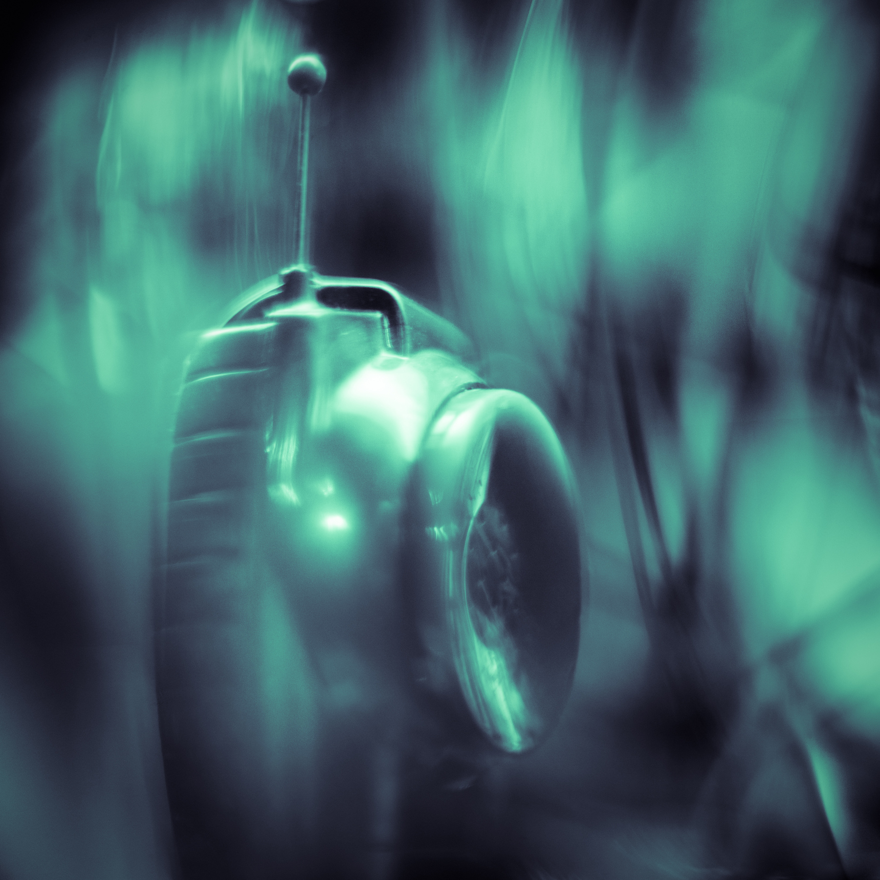 A metallic object with a rounded shape and a small antenna on top, set against a blurred greenish background.
