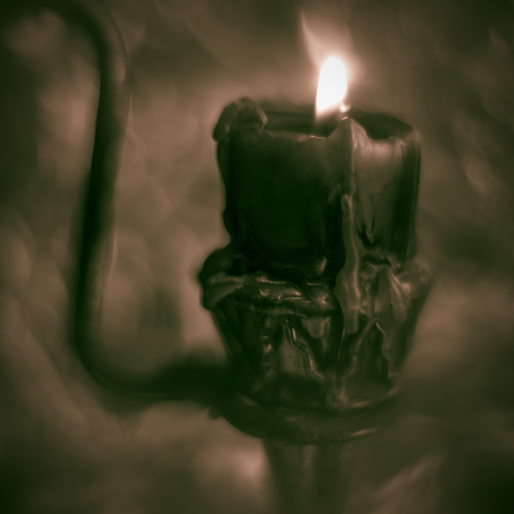 A lit candle with melted wax on a dark surface, with a blurred background.