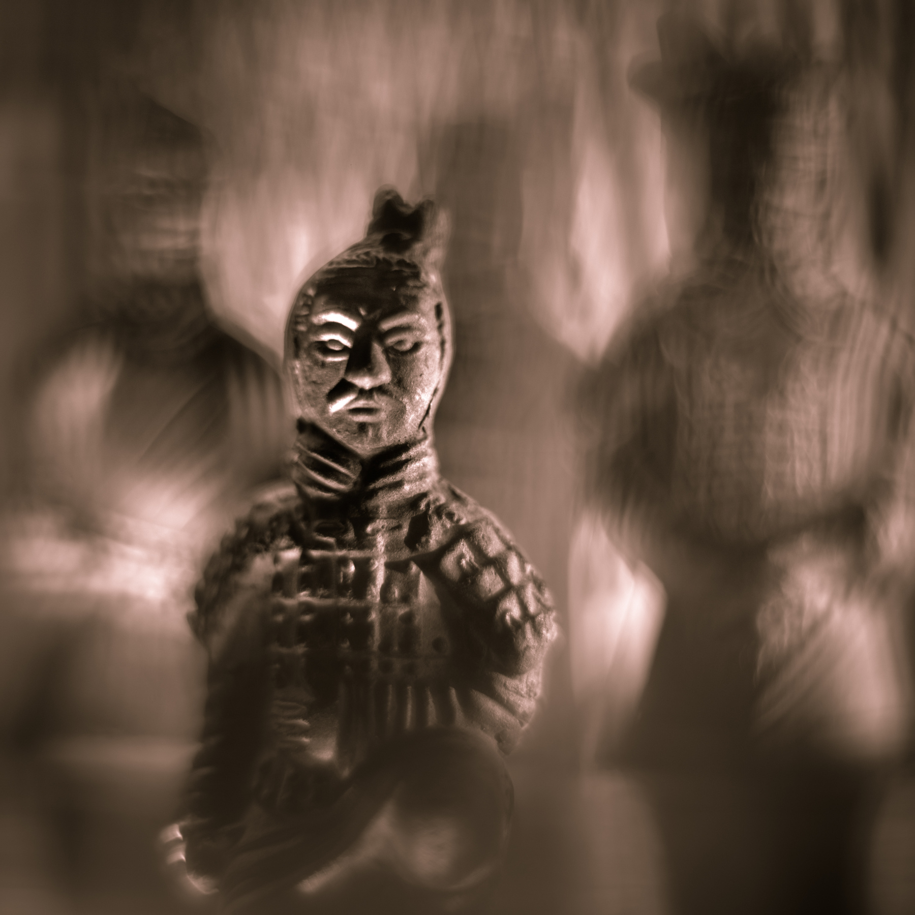 A statue of a person with detailed clothing and a headdress, surrounded by blurred figures, in sepia tone.