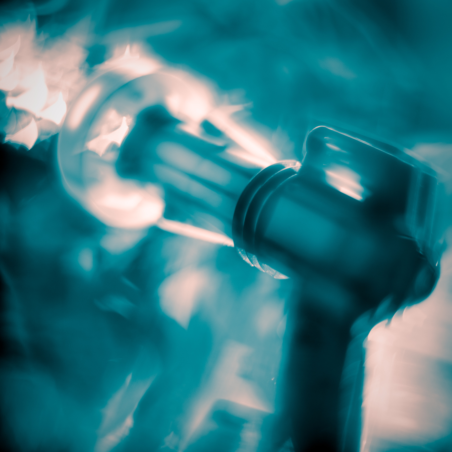Close-up of a hand holding a spray bottle, with a blurred background and mist, in a teal color tone.