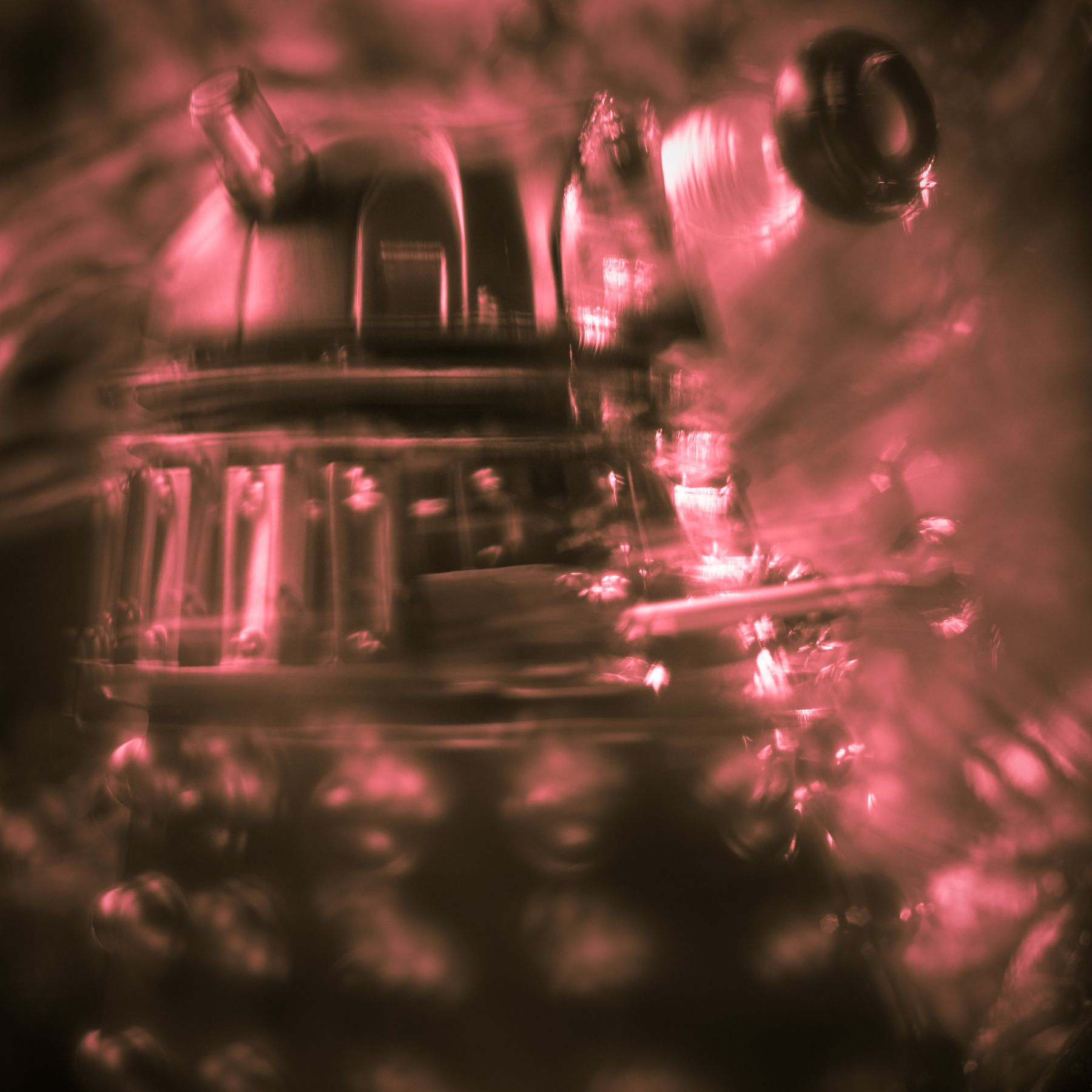 Blurred image of a robot or machine with a dome-shaped top and various components, in a pinkish hue.